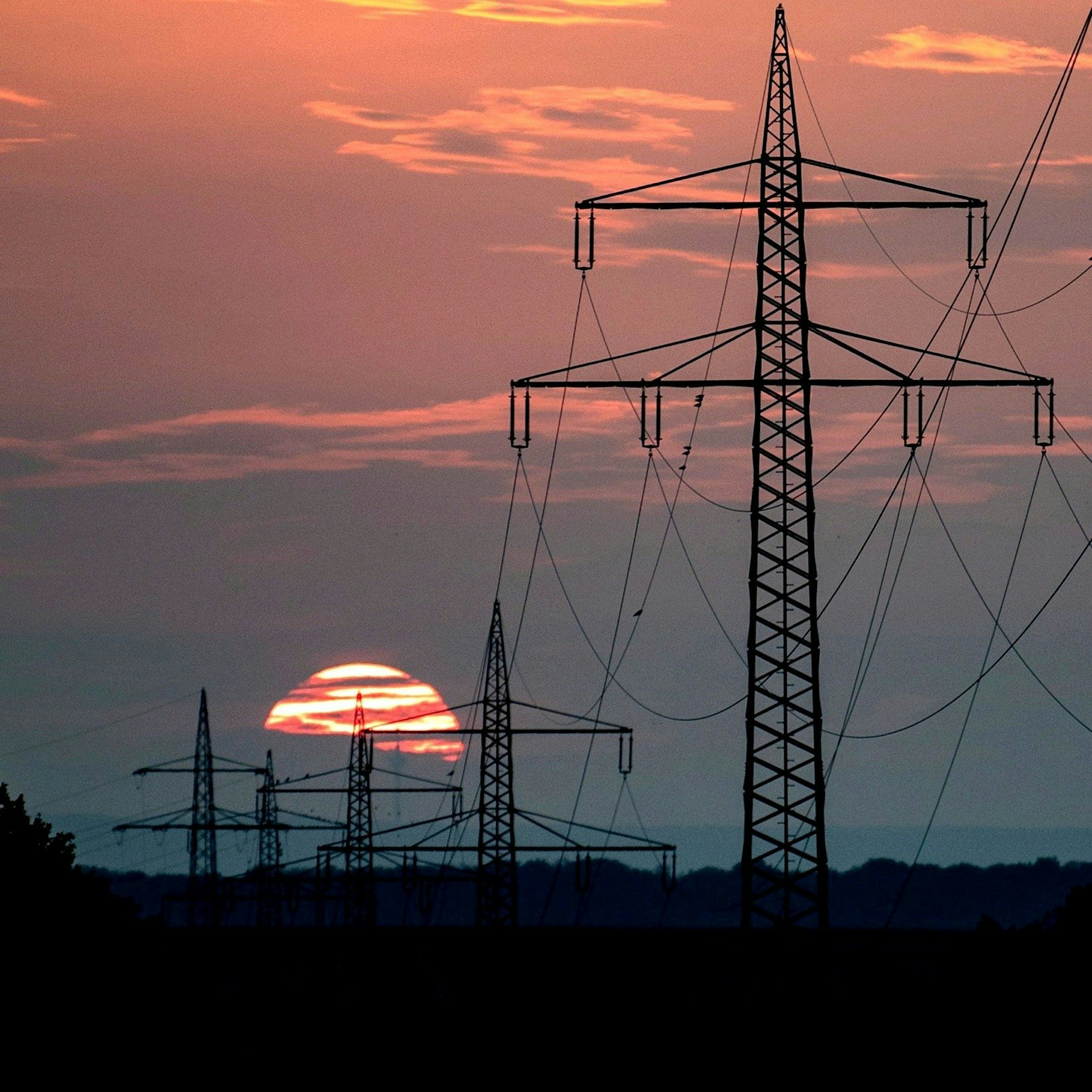 Masten und Drähte einer Hochspannungsleitung sind vor der untergehenden Sonne zu sehen.