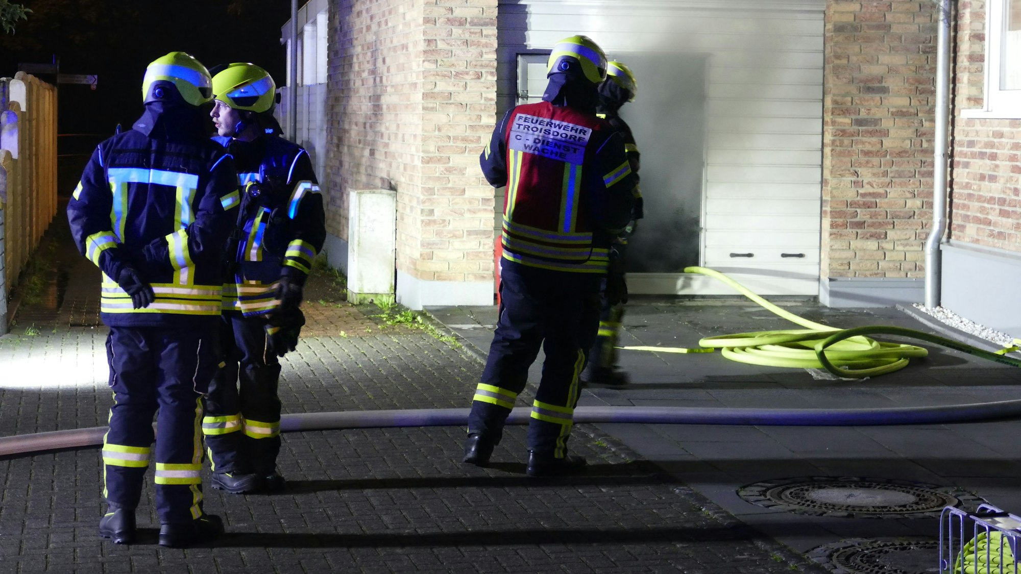 Feuerwehrleute stehen vor einer Garage, aus der Qualm dringt.