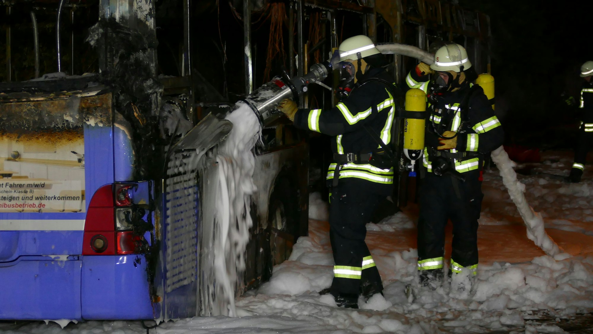 Feuerwehrleute löschen einen Bus mit Schaum.