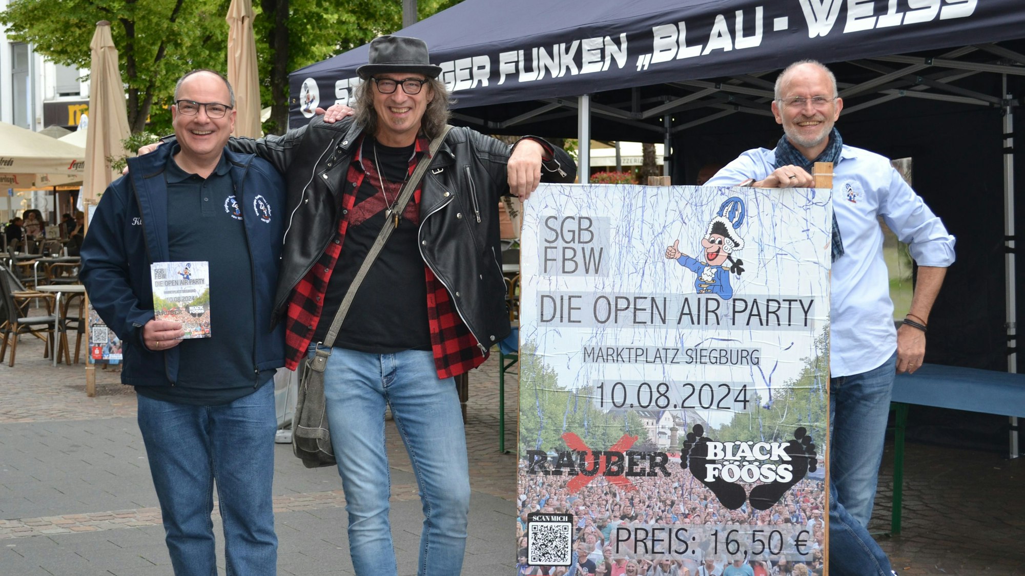 Drei Männer stehen neben einem Plakat, das für eine Open-Air-Party wirbt.