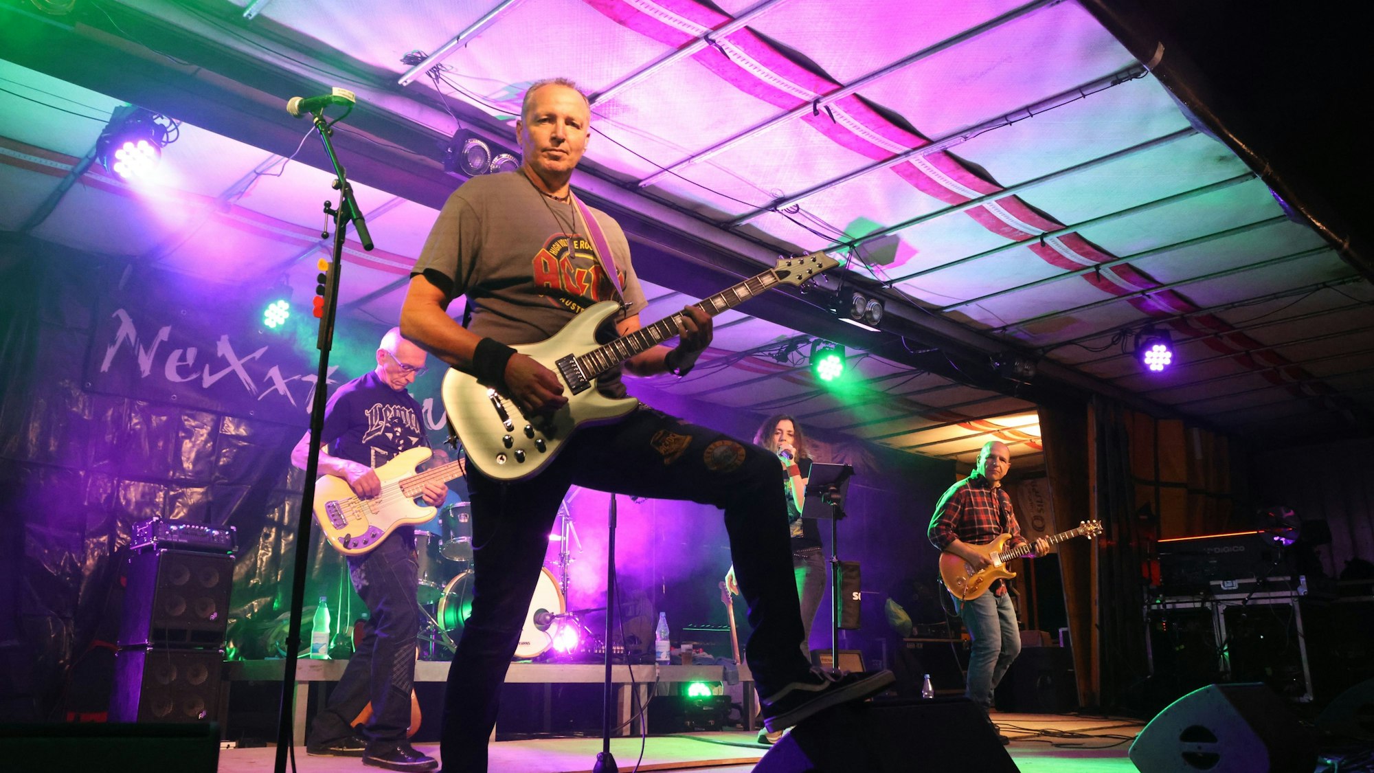 Die Musiker der Gruppe Nexxt Level auf der Bühne, der Frontmann hat eine Gitarre in Händen und schaut in die Kamer.