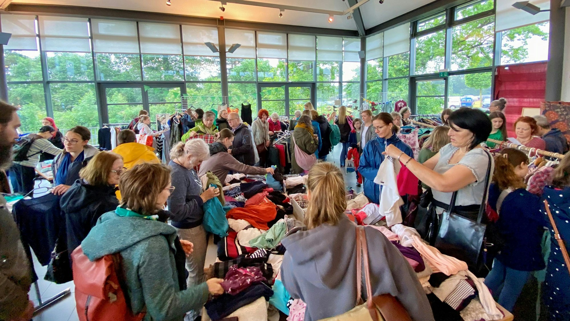 Viele Menschen stöbern in Kleidung, die auf Tischen ausliegt.
