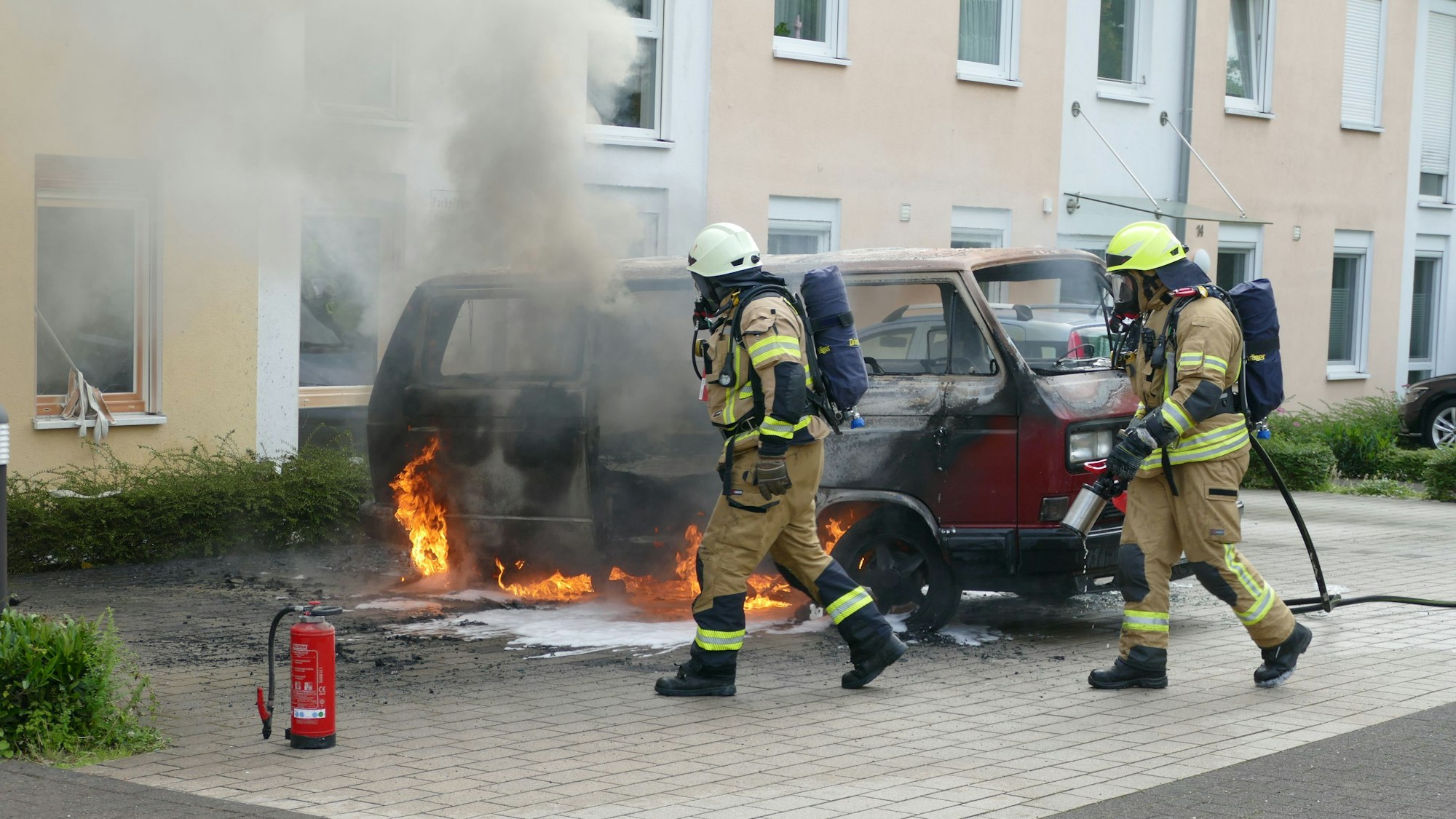 Feuerwehrleute vor einem brennenden Auto.