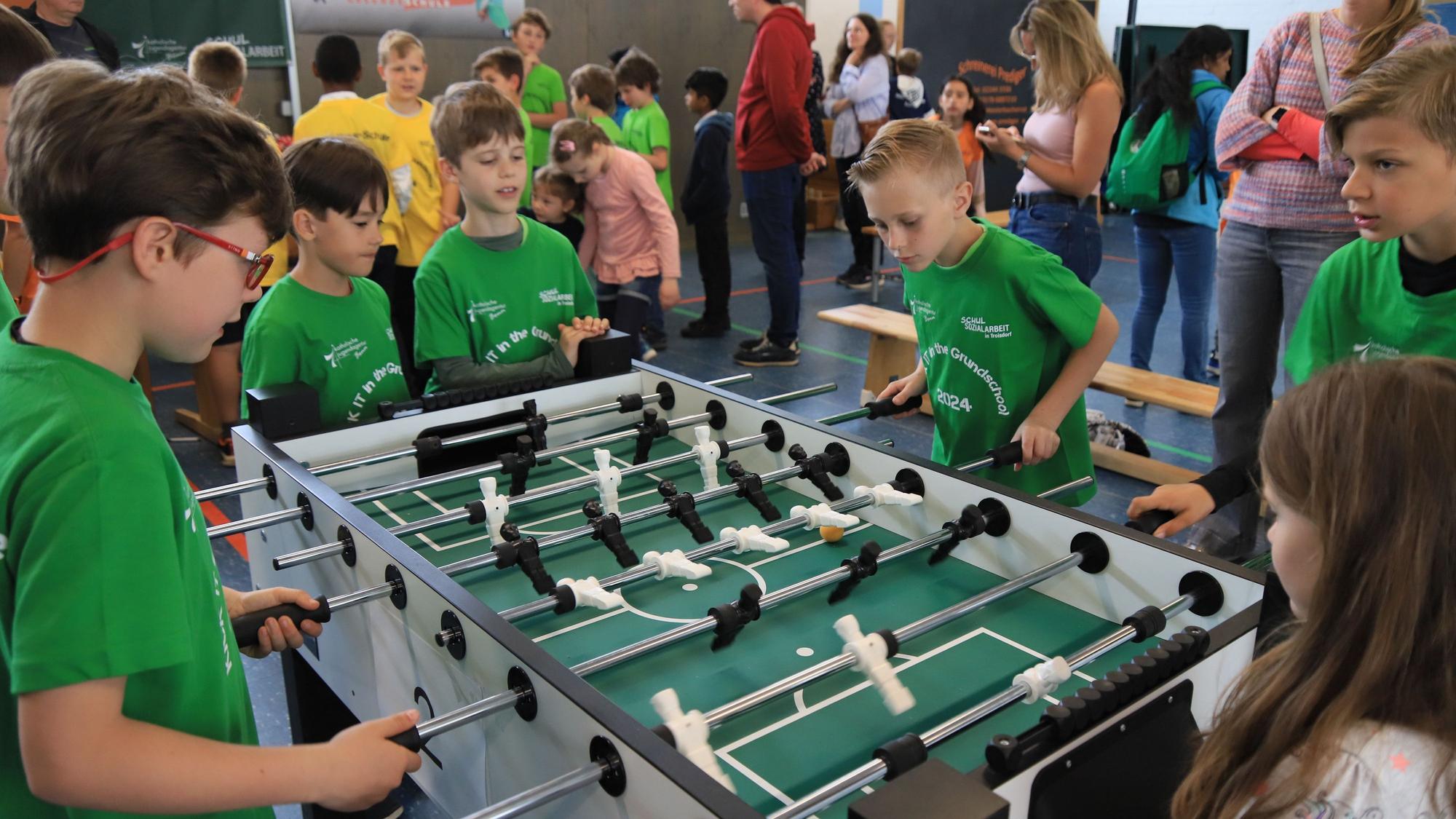 Jungen in grünen T-Shirts an einem Tischfußballtisch.