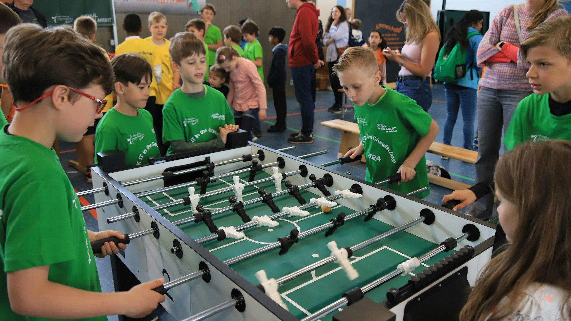 Jungen in grünen T-Shirts an einem Tischfußballtisch.