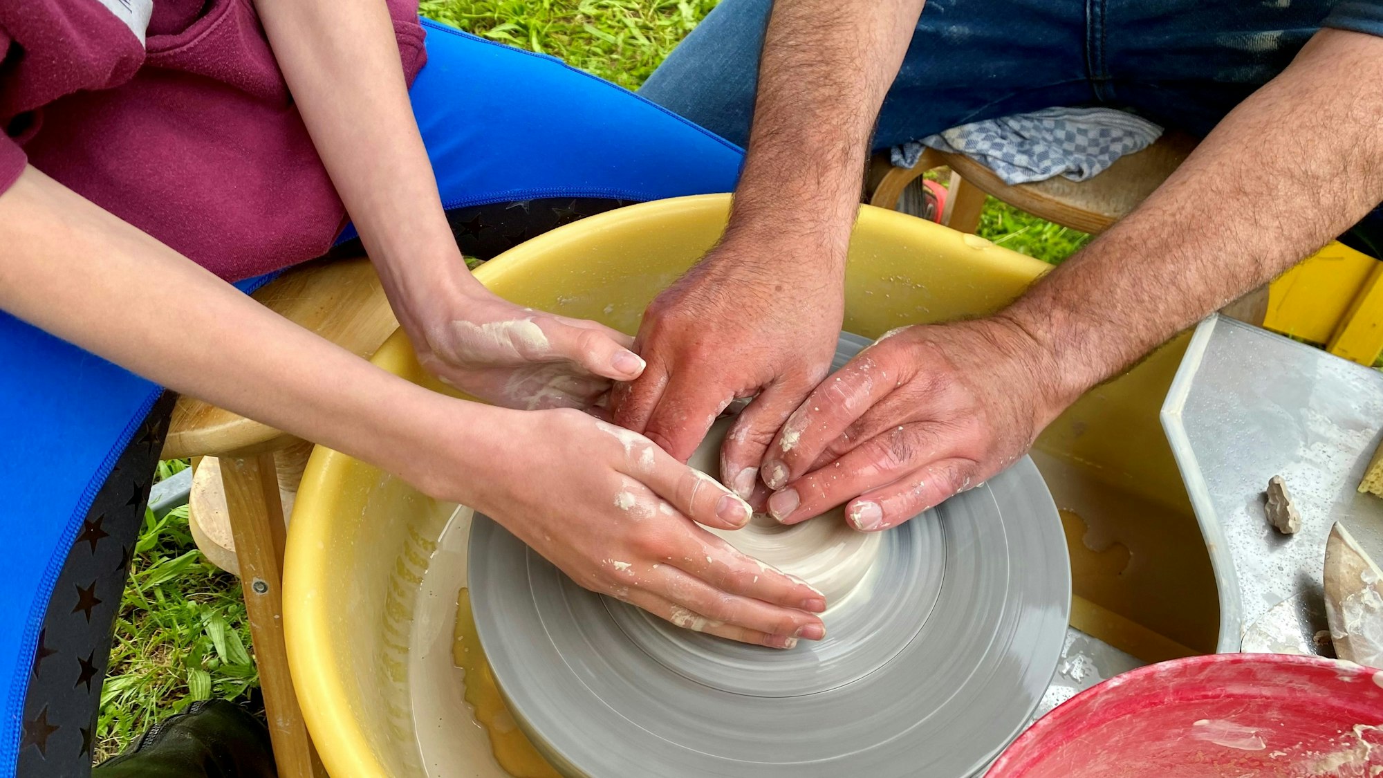 Zwei Paar Hände arbeiten mit Ton auf einer Töpferscheibe.