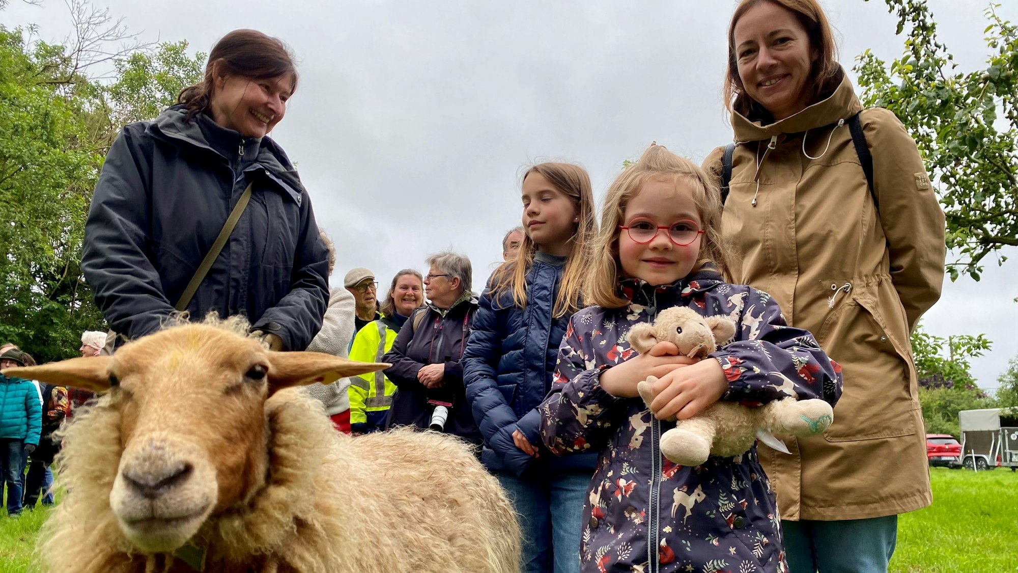 Ein Mädchen mit einem Kuschelschaf im Arm posiert neben einem echten Schaf.