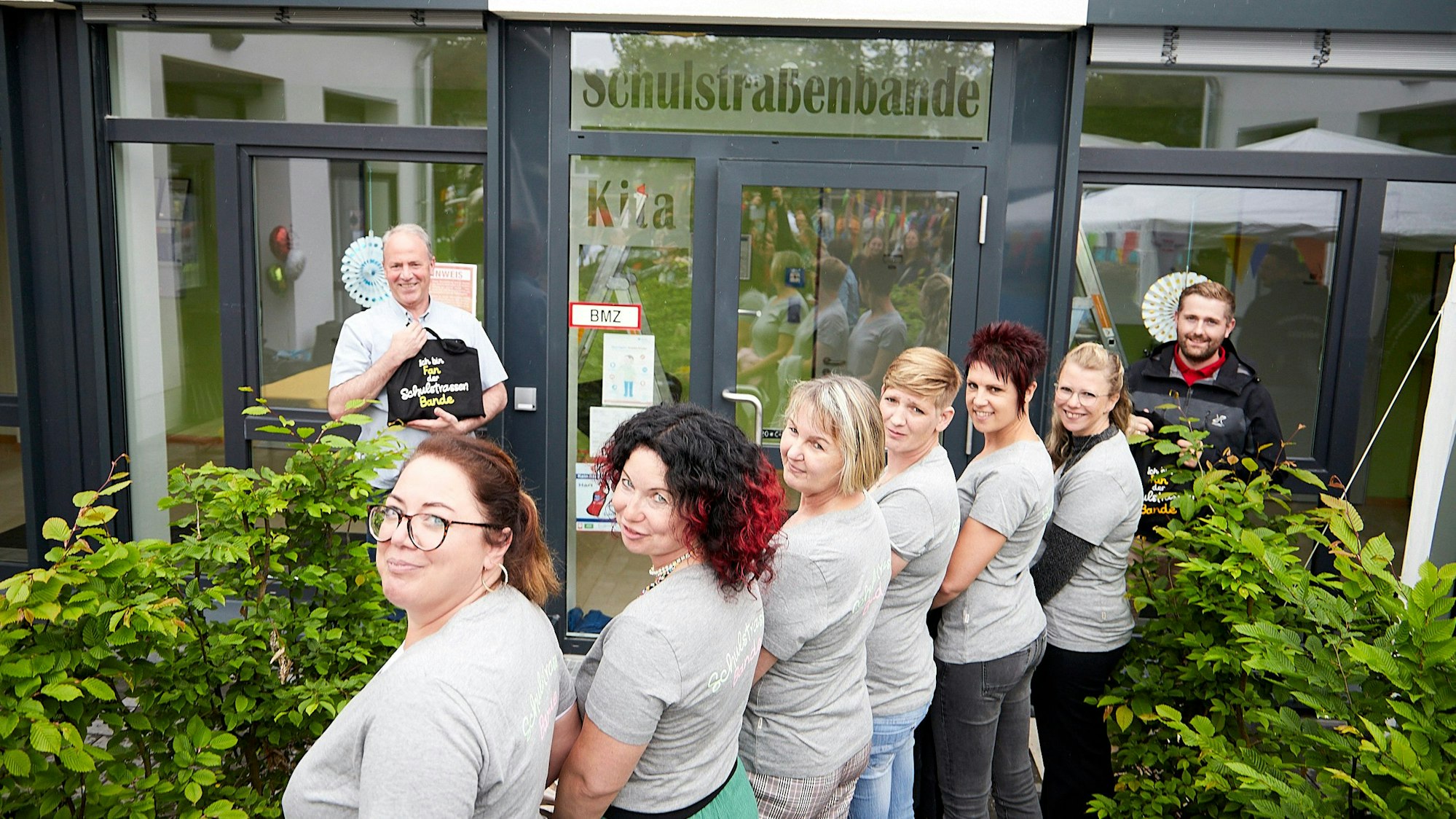 Zwei Männer stehen an der Tür zum Kindergarten in Sötenich. Sie haben den über der angebrachten Namen enthüllt. Davor stehen die sechs Erzieherinnen der Kita.