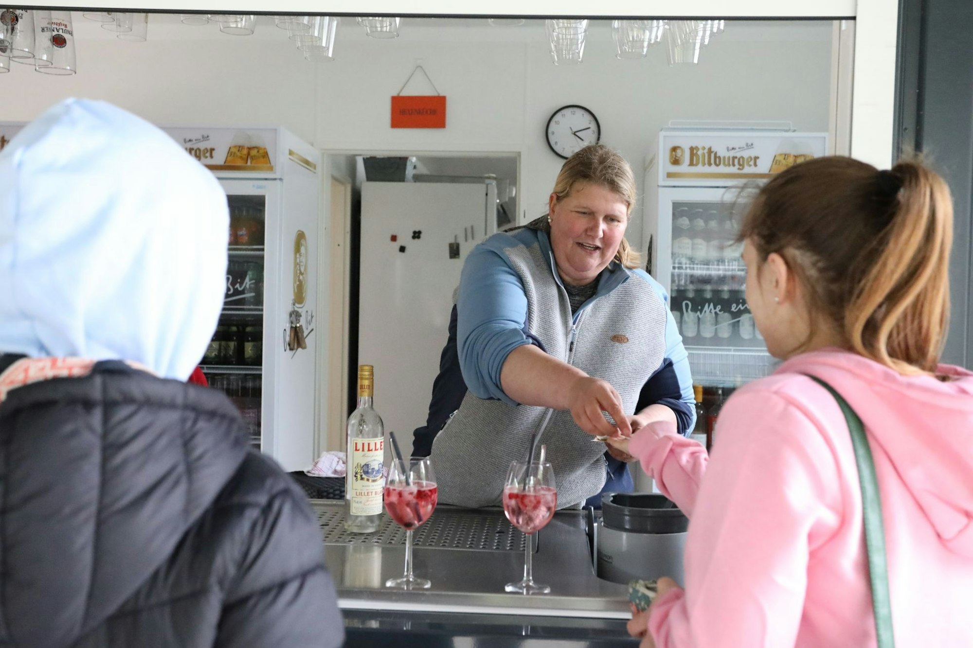 Eine Frau an einer Theke bedient zwei Kunden.
