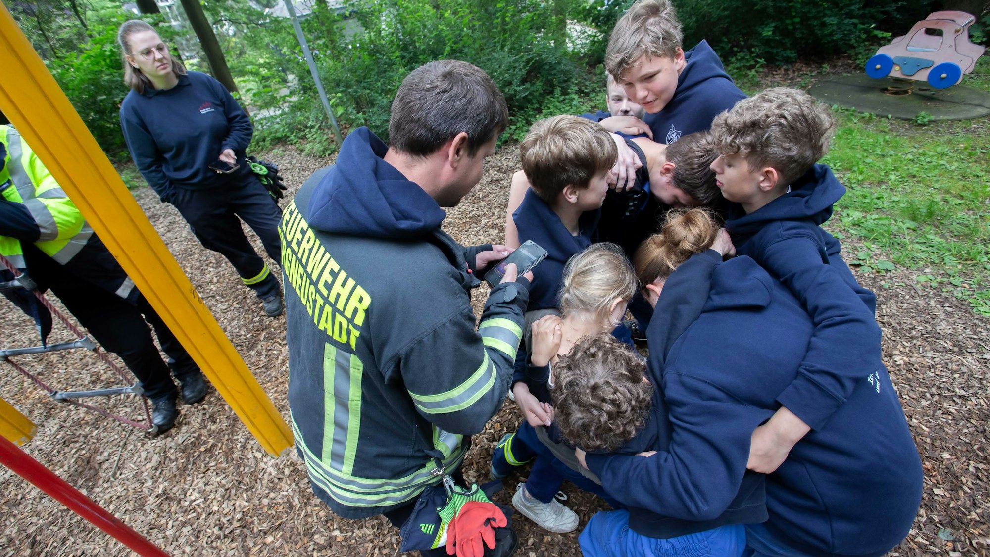 Eine Gruppe Kinder und Jugendlicher in Feuerwehrkleidung umarmt sich und steht eng in einem Kreis zusammen.