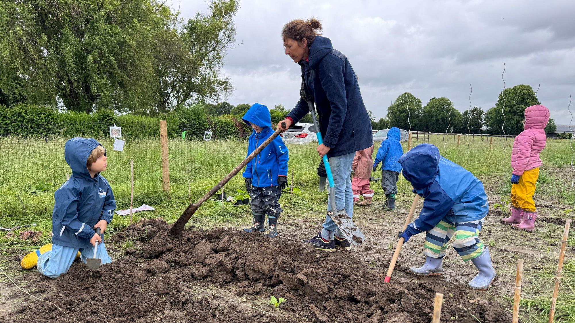 Auf dem Bild ist eine Waldpädagogin zu sehen, die Kita-Kindern zeigt, wie Bohnen gepflanzt werden.