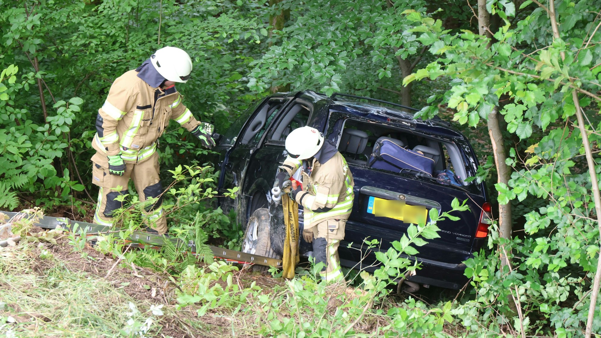 Kräfte der Feuerwehr sichern ein nach einem Unfall abgerutschtes Auto mit Stahlseilen für die Bergung.
