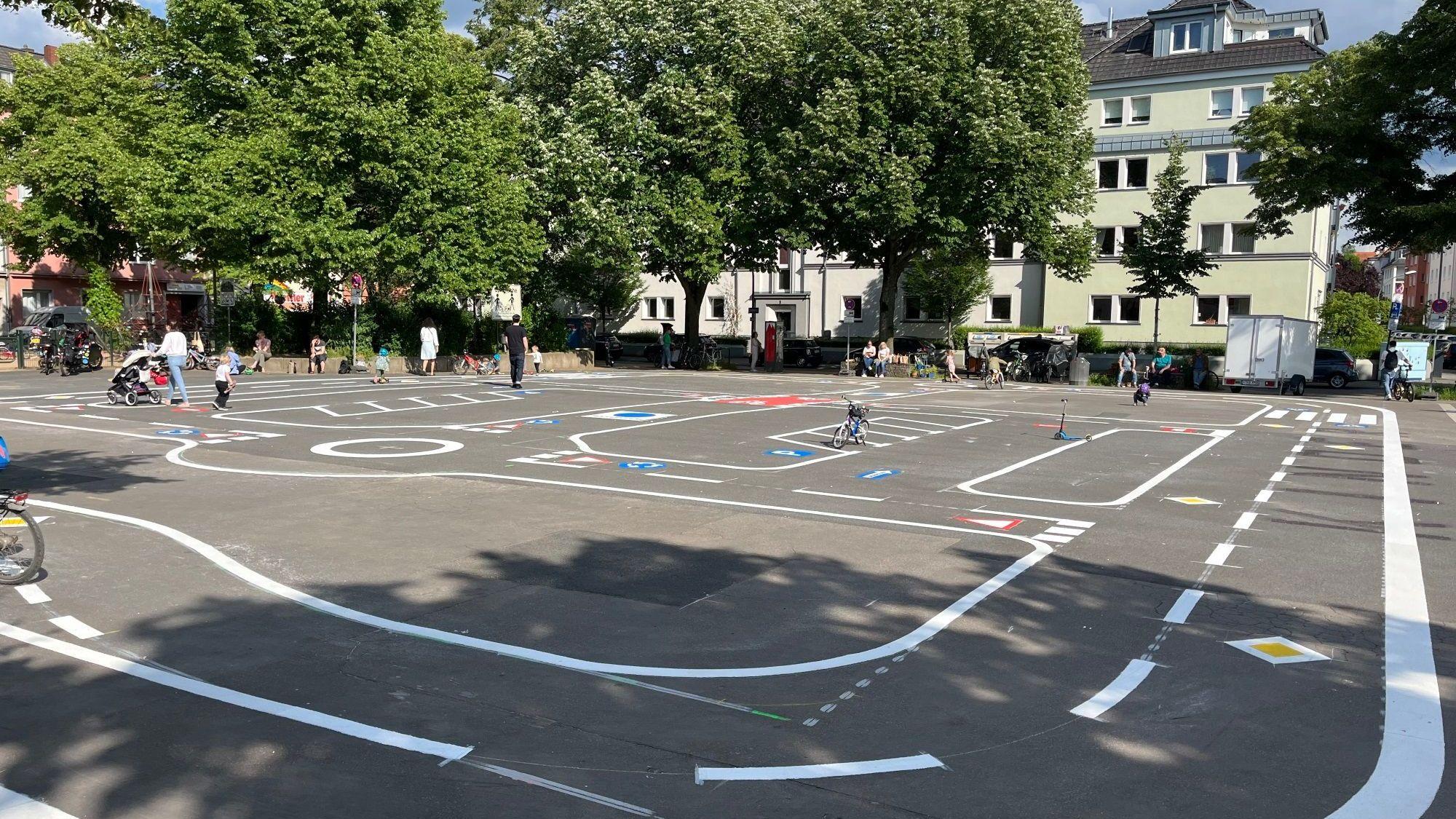 Eine Betonfläche mit Fahrbahnmarkierungen und Verkehrsschildern auf dem Boden, Kinder spielen
