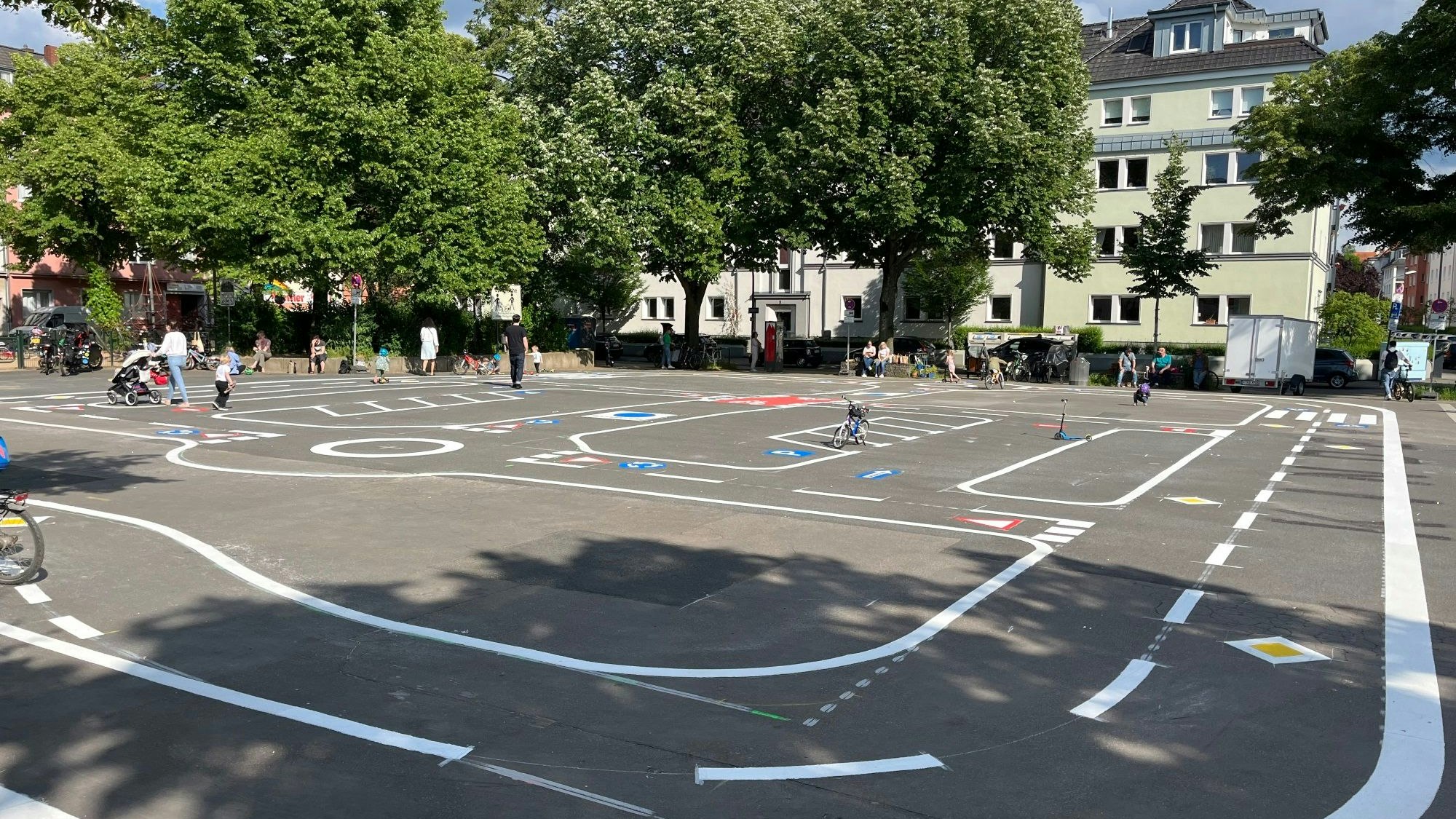 Eine Betonfläche mit Fahrbahnmarkierungen und Verkehrsschildern auf dem Boden, Kinder spielen