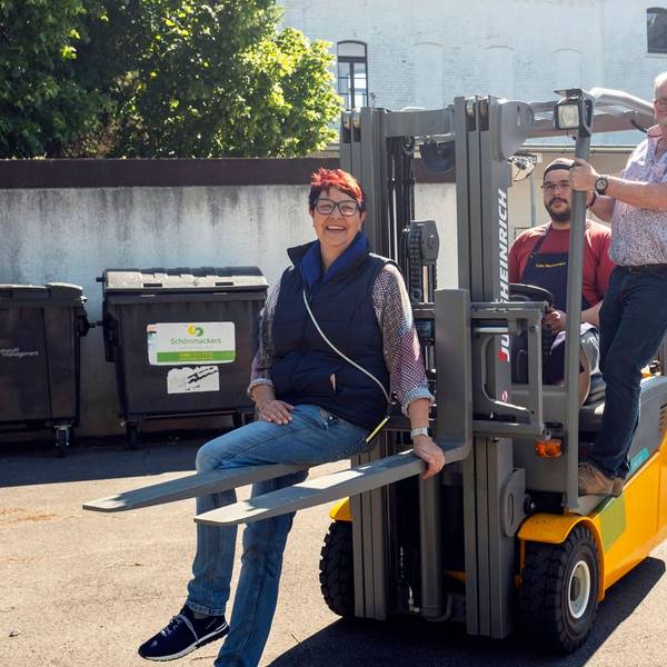 Manuela Pütz, Fahrer Tim Achnitz und Wolfgang Weilerswist posieren auf einem Gabelstapler fürs Foto.