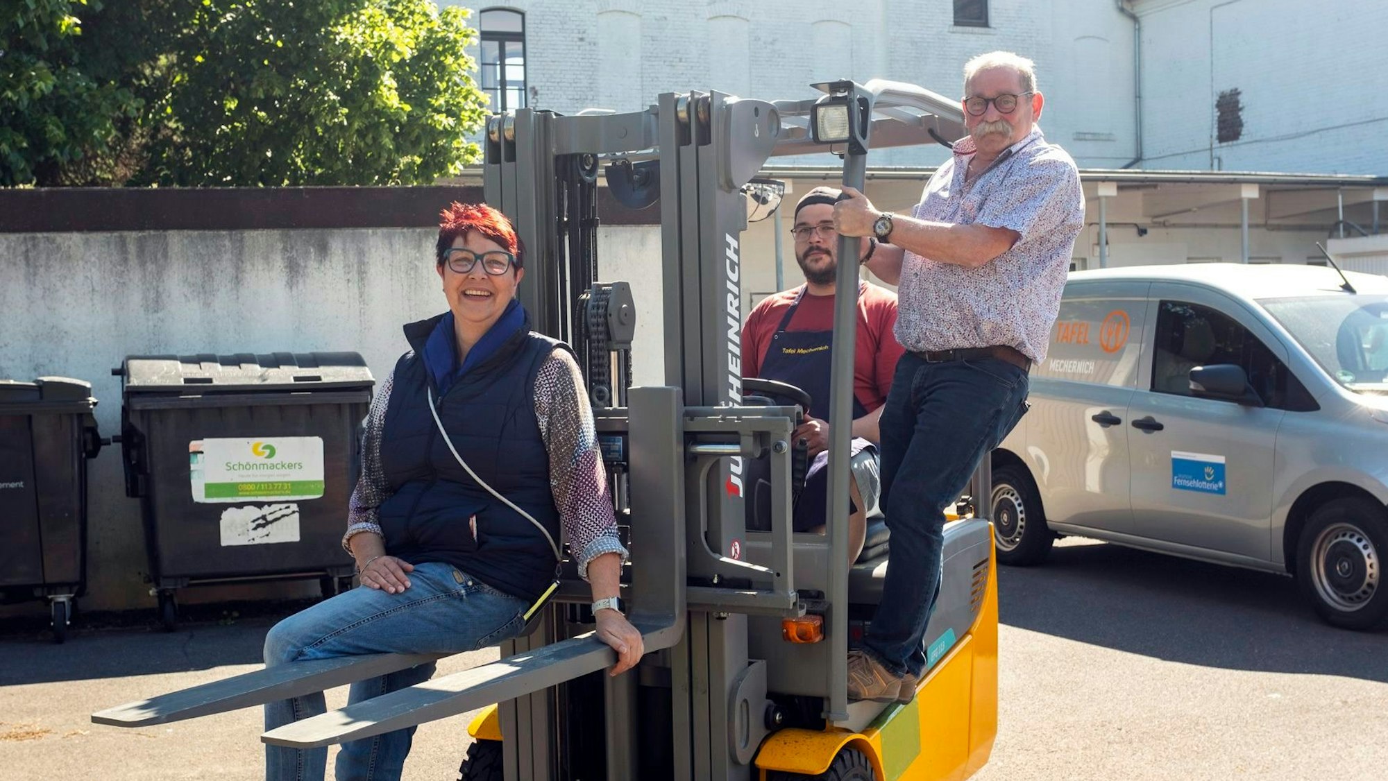 Manuela Pütz, Fahrer Tim Achnitz und Wolfgang Weilerswist posieren auf einem Gabelstapler fürs Foto.