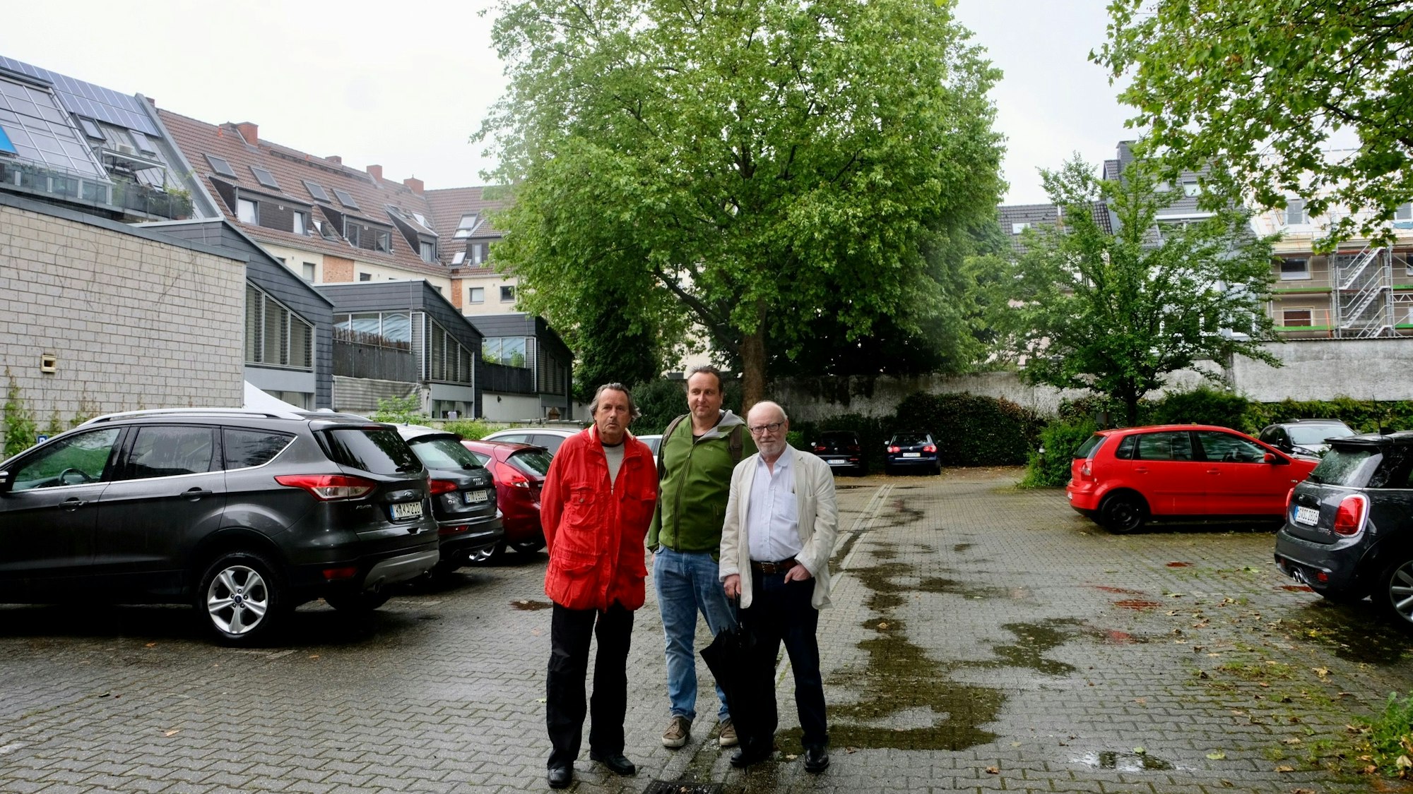 Die Bezirksvertreter Roland Schüler, Florian Weber-Baronowsky (Grüne) und Friedhelm Hilgers stehen auf dem Parkplatz an der Redwitzstraße 62 in Köln-Sülz und vor der großen Platane im Hintergrund. Foto von Susanne Esch.