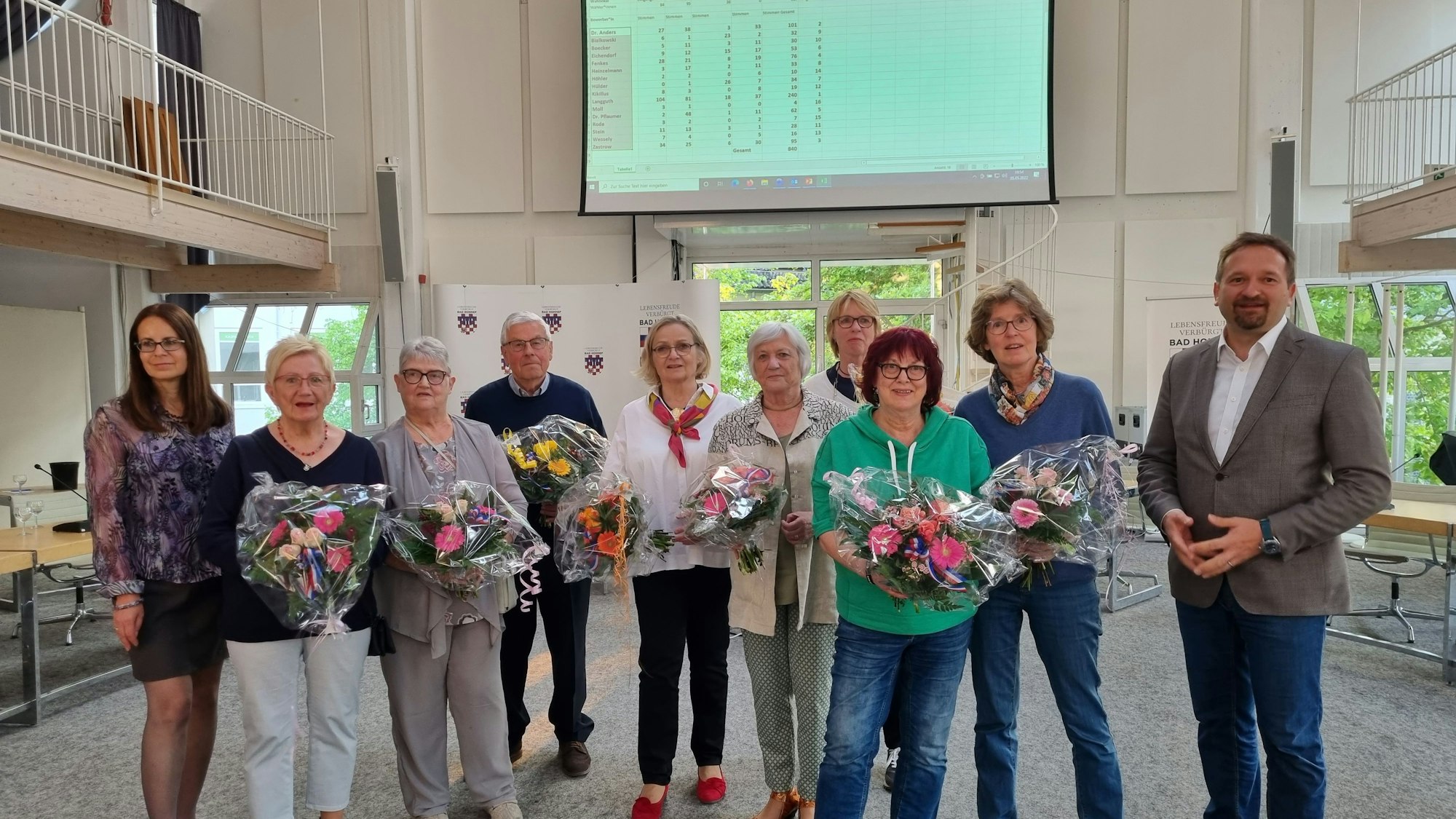 Eine Gruppe von Männern und Frauen stehen nebeneinander, viele halten Blumensträuße in den Händen.