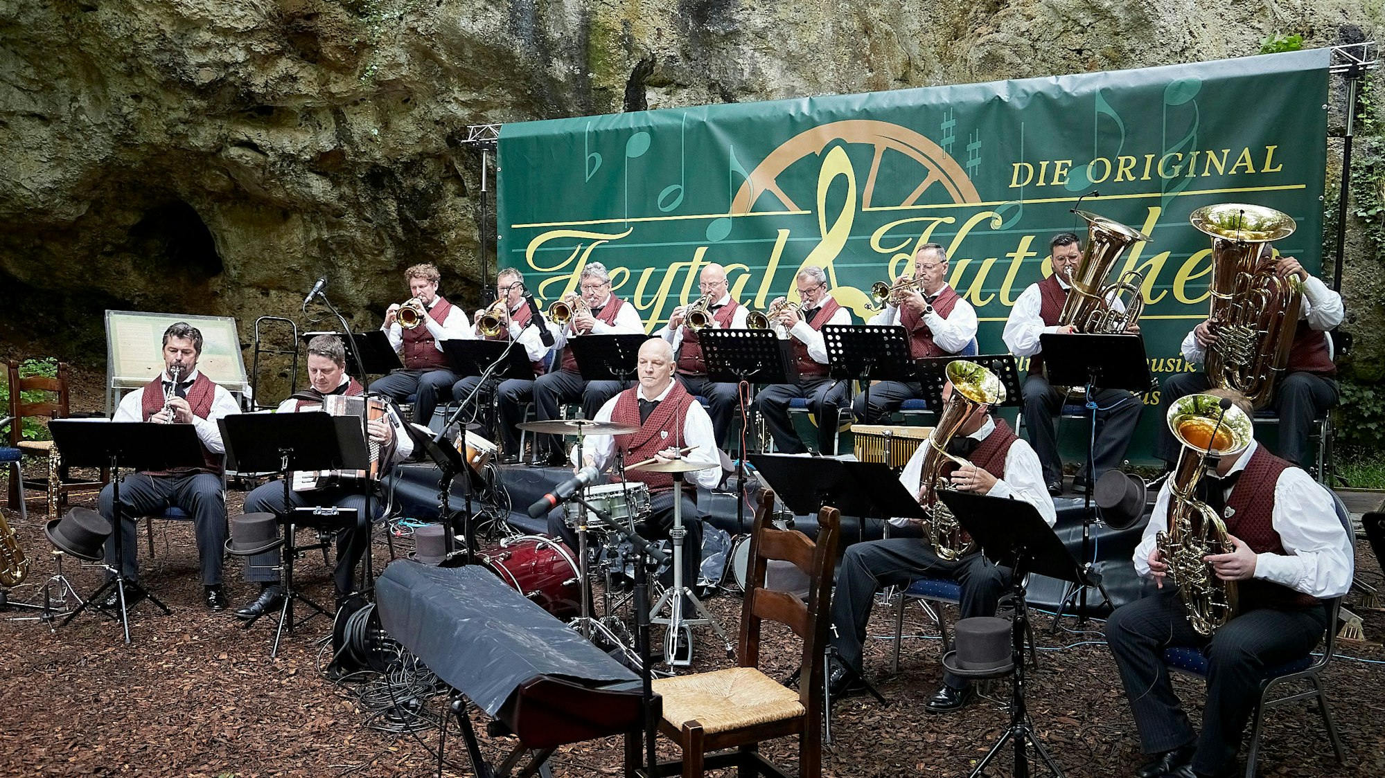Die Musikanten der Feytal-Kutscher sitzen vor der Kakushöhle in Mechernich auf ihren Stühlen und spielen auf ihren Blasinstrumenten.