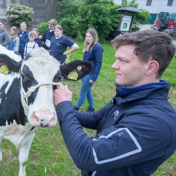 Während eines Camps stehen Kinder und Jugendliche auf einer Wiese nahe einer Kuh, die von einem jungen Mann an einem Strick festgehalten wird.