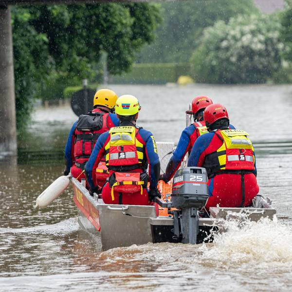 DLRG-Retter fahren mit einem Motorboot auf einer überfluteten Straße.