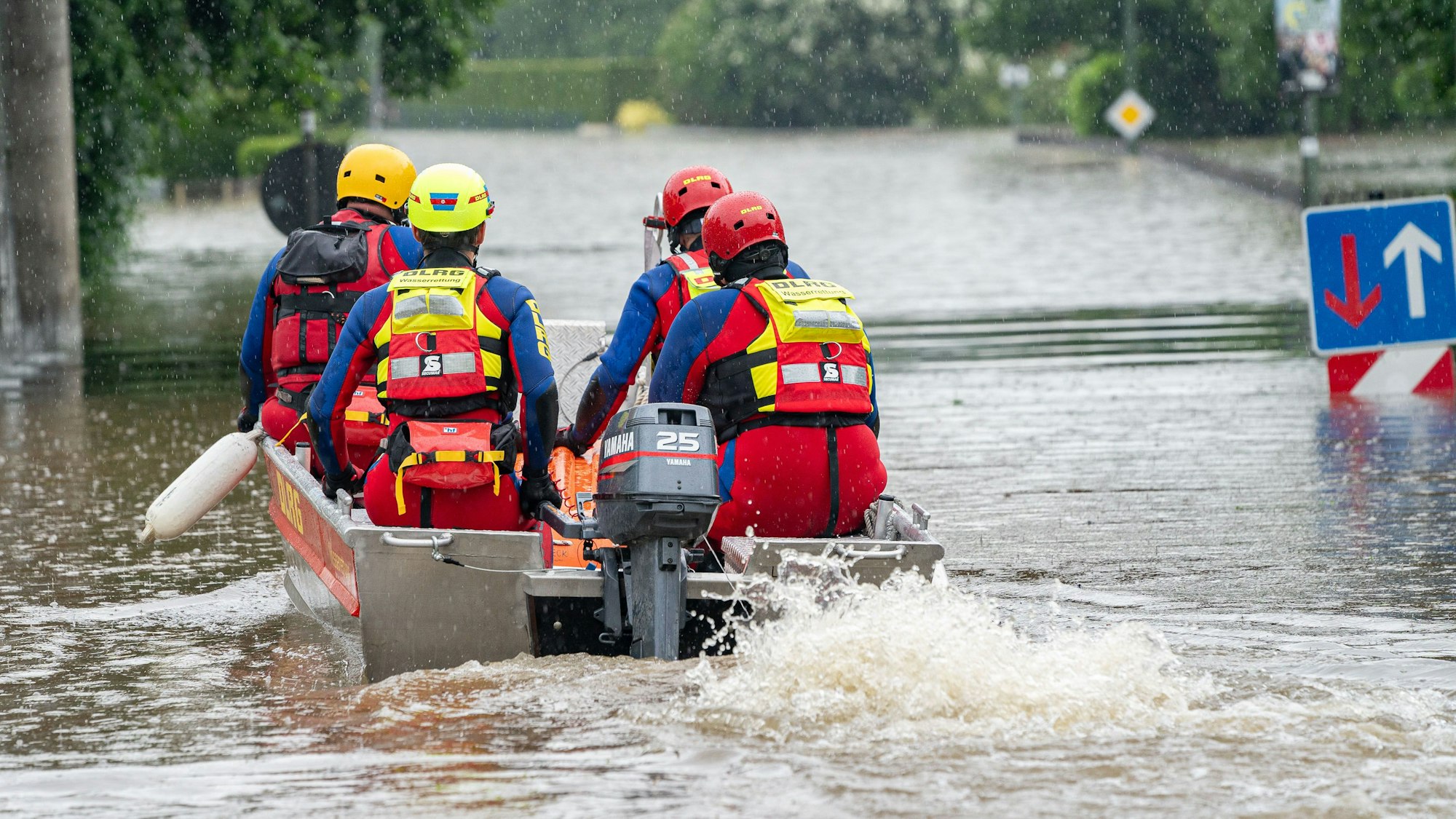 DLRG-Retter fahren mit einem Motorboot auf einer überfluteten Straße.
