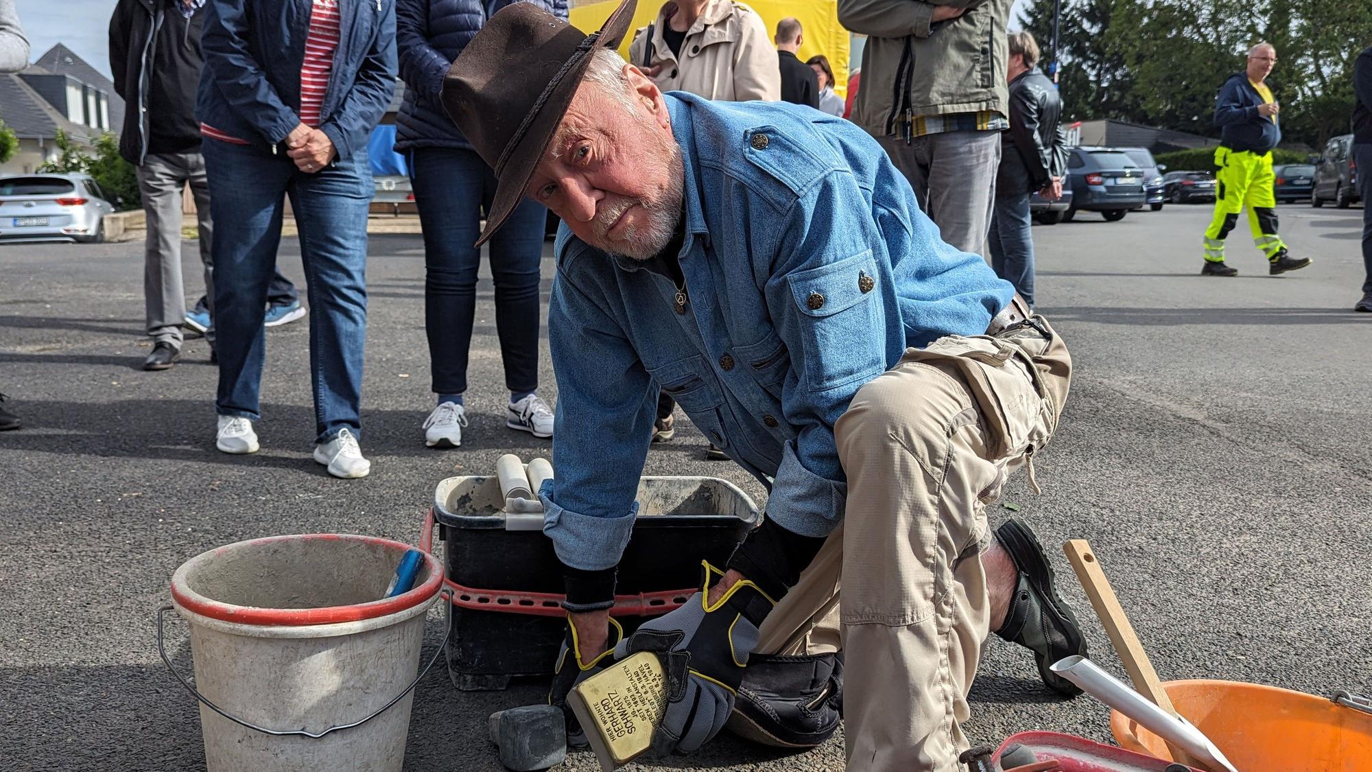 Der Künstler Gunter Demnig lässt den Stolperstein in den Asphalt ein. Neben ihn ein Eimer mit Zement.