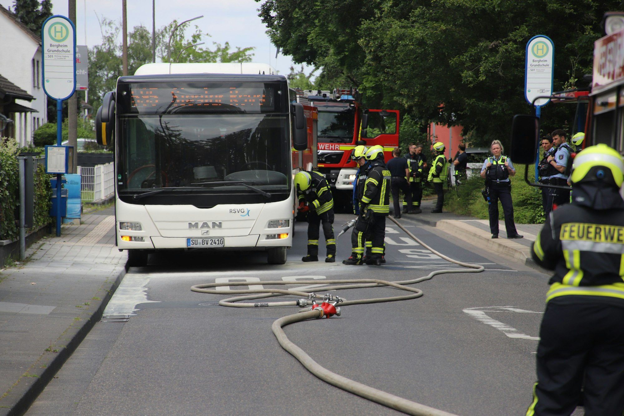 An einem Linienbus tehen Feuerwehrleute und kühlen die heiß gelaufenen Bremsen mit einem Wasserschlauch..