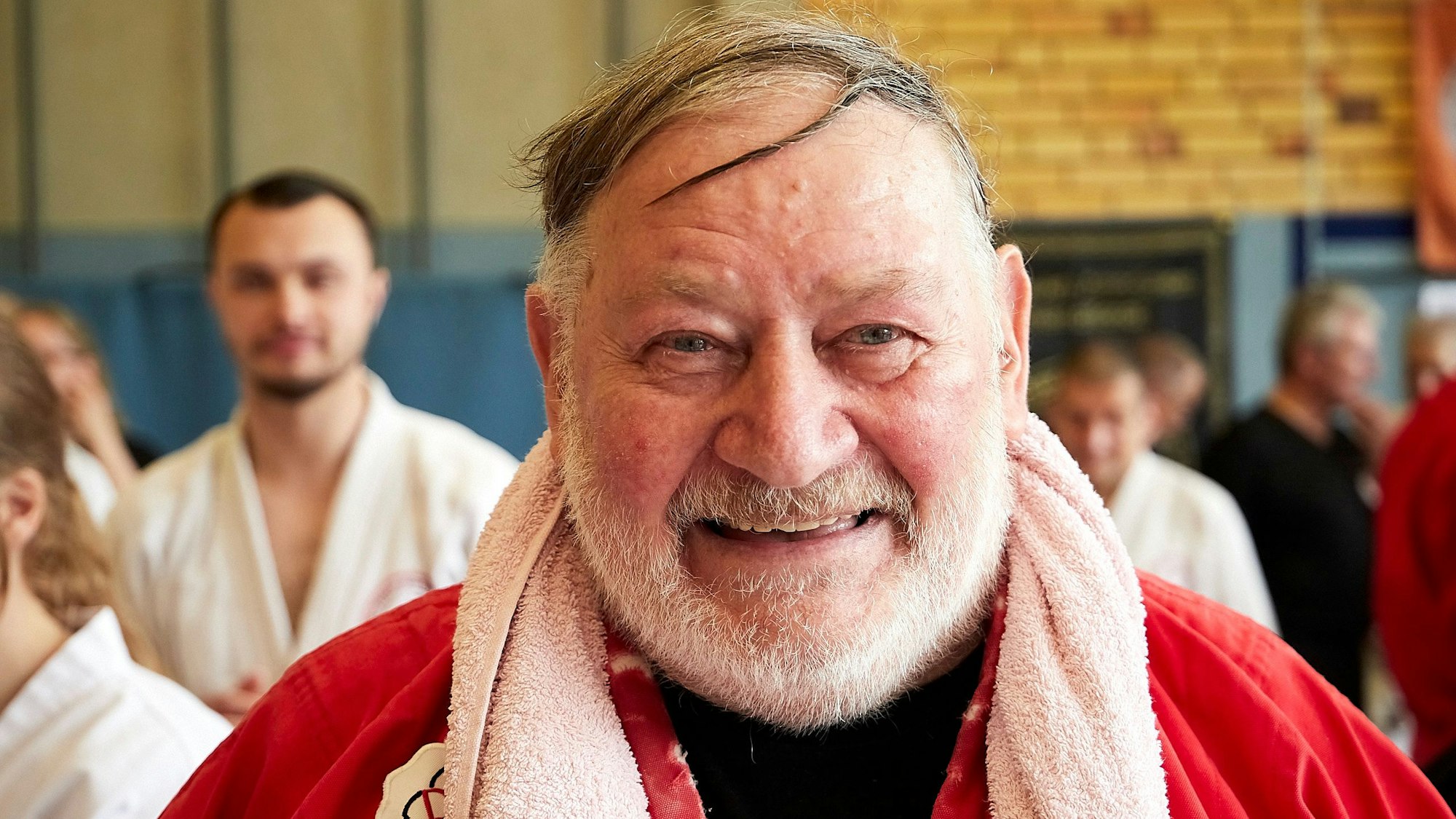 Heinrich Drosten steht in einer Sporthalle und hat ein Handtuch um den Hals gelegt. Er ist Kampfsportler, Träger des 10. Dan und seit 70 Jahren auf der Matte aktiv.