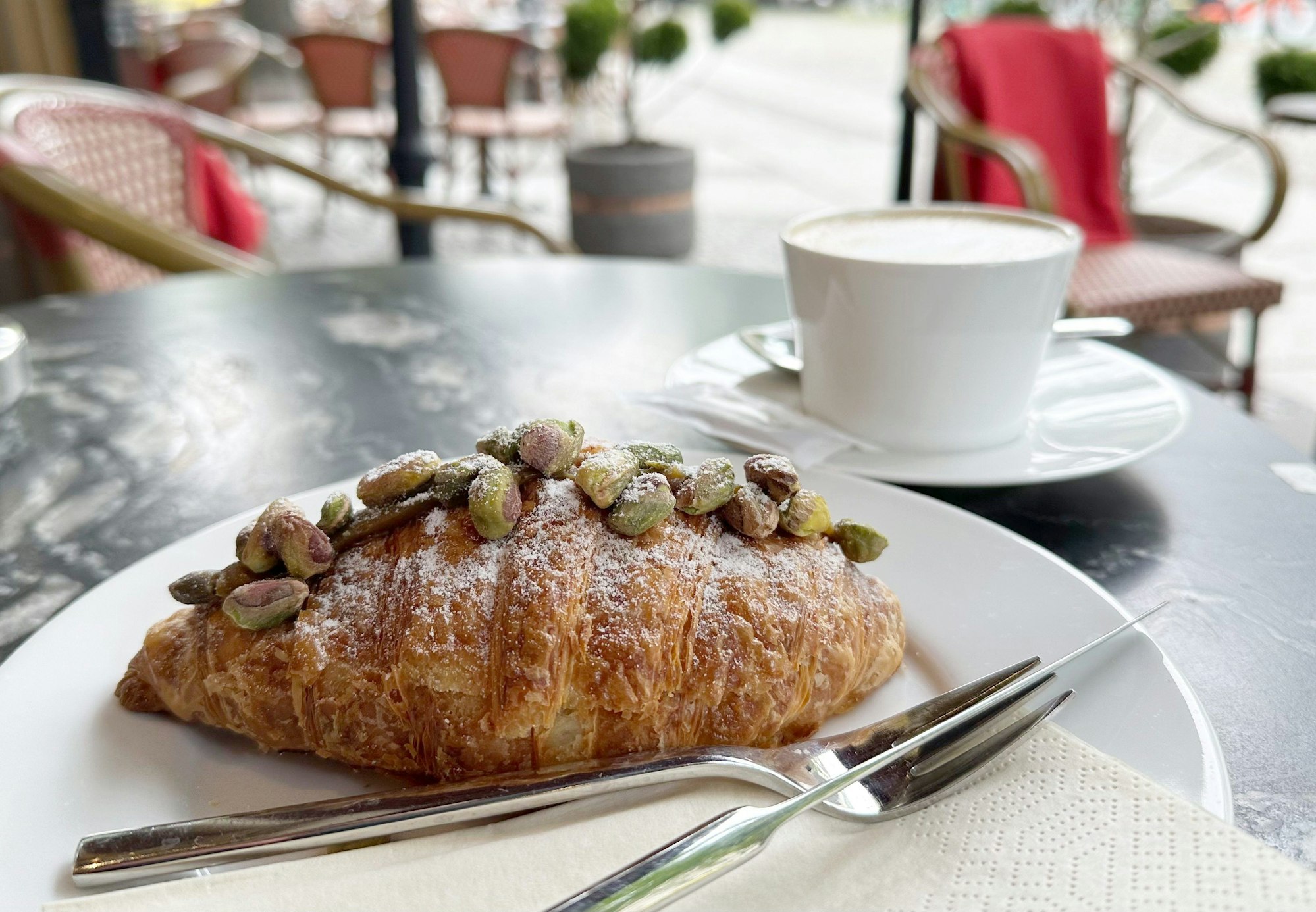 Ein Pistazien-Croissant liegt auf einem Teller in einem Café.