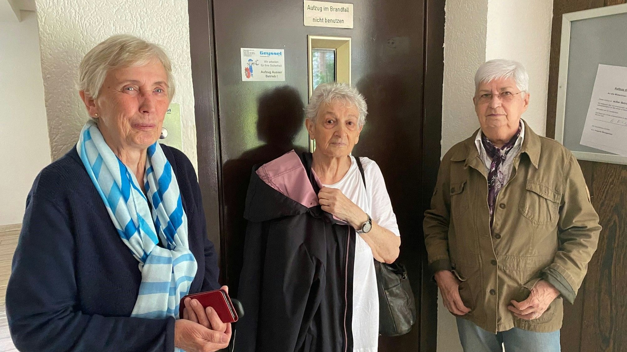 Zu sehen sind drei der Bewohner vor der verschlossenen Aufzugstür.