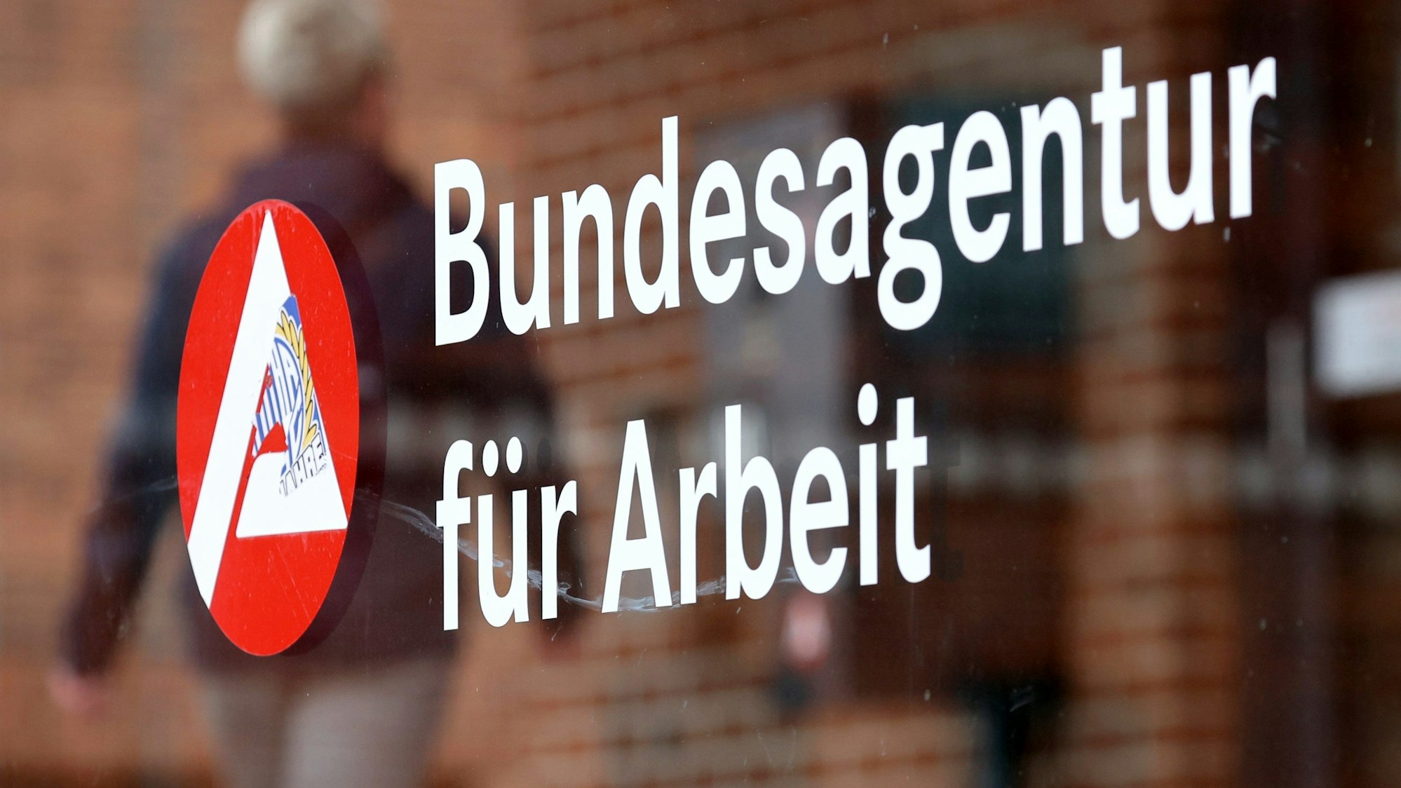Ein Mann geht an einem Schild mit der Aufschrift „Bundesagentur für Arbeit“ vorbei.
