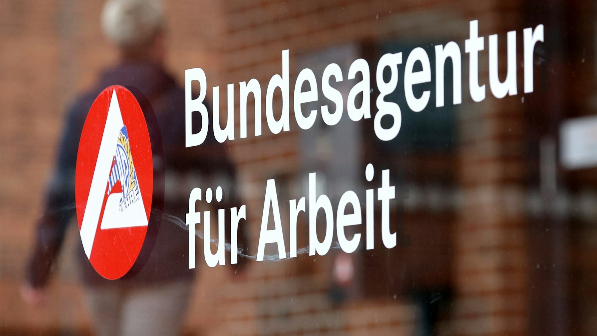 Ein Mann geht an einem Schild mit der Aufschrift „Bundesagentur für Arbeit“ vorbei.
