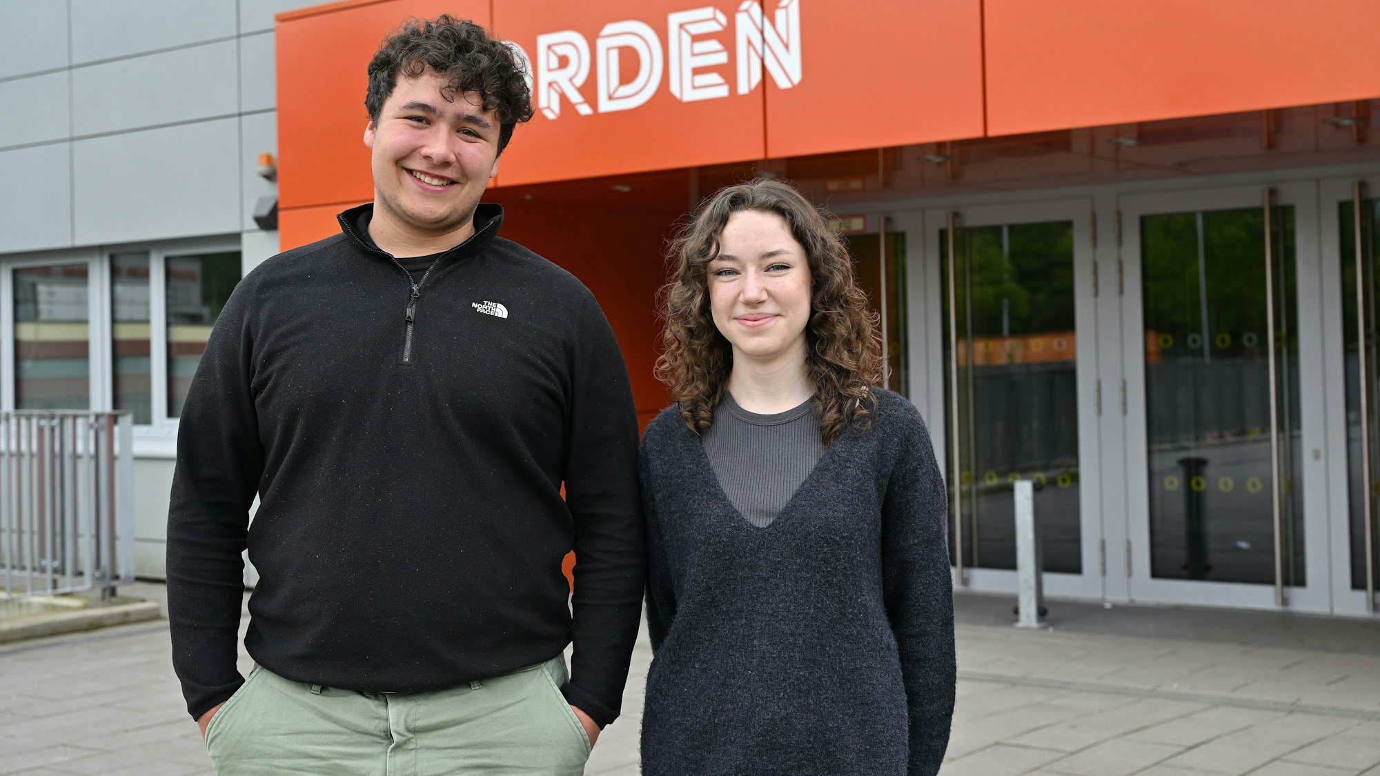 Die beiden Schüler stehen nebeneinander vor dem Eingang zum Schulgebäude.