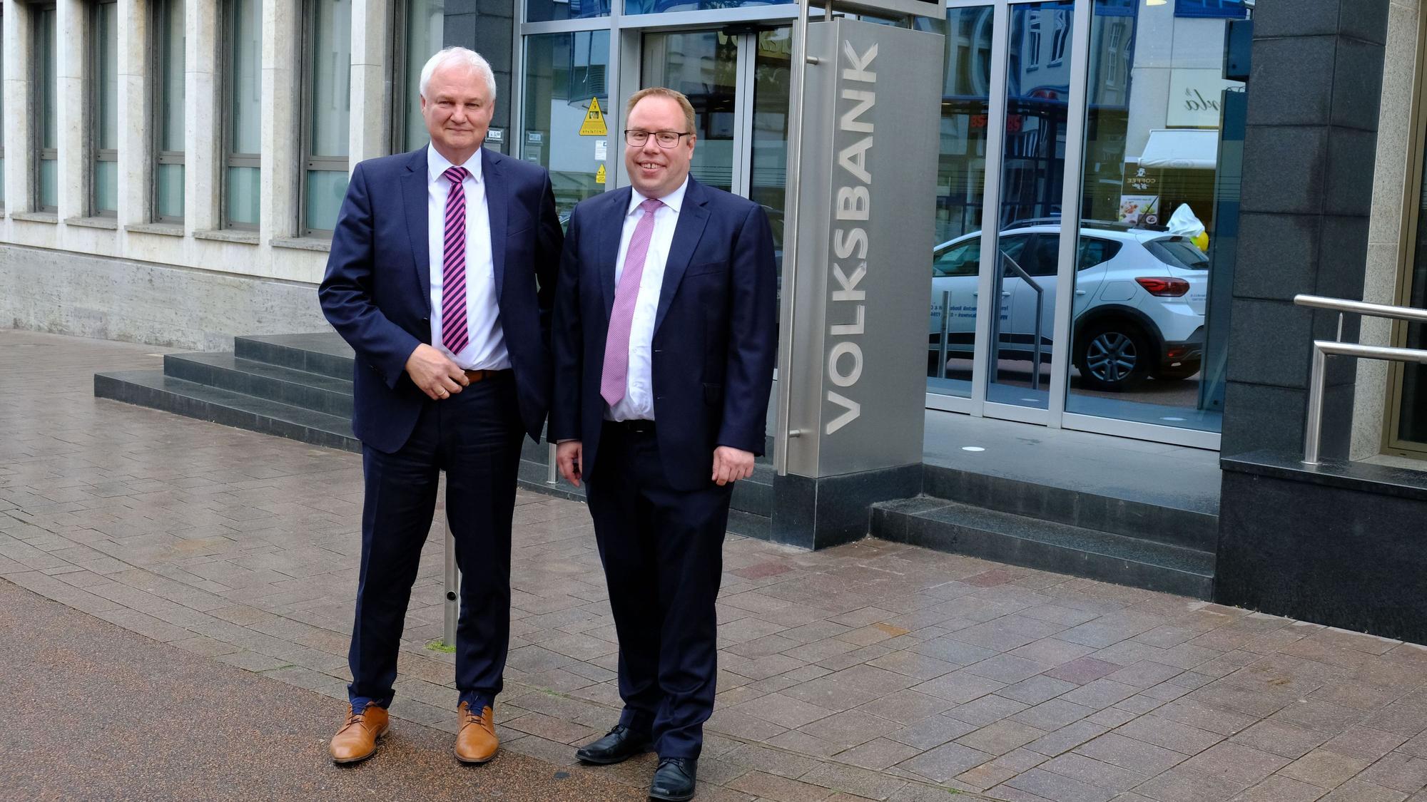 Hans-Jürgen Lembicz (l.) und Marc Güttes stehen in Anzügen vor der Volksbank-Filliale in Euskirchen.