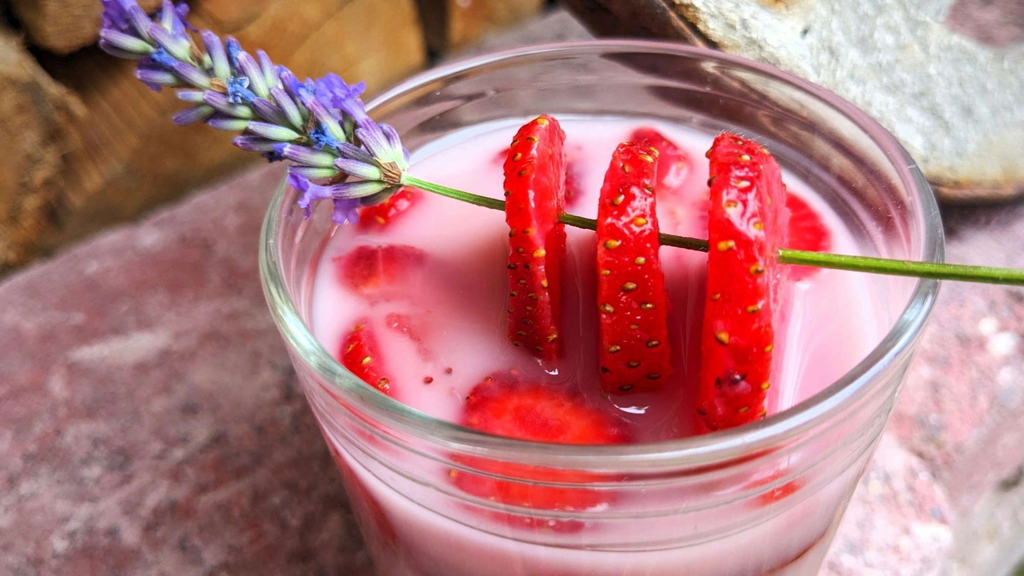 Ein Lavendelzweig mit drei aufgespießten Erdbeerscheiben dekorieren das Glas mit dem Getränkt.