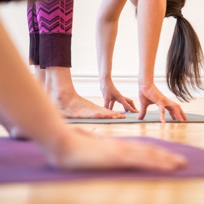 eine Frau steht auf einer Yogamatte und berührt mit ihren Händen den Boden.