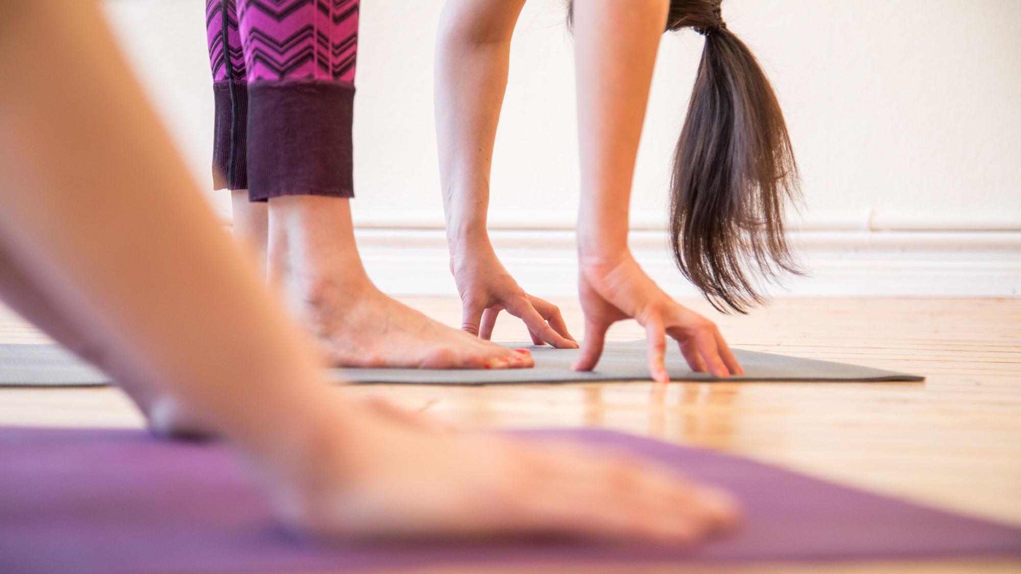 eine Frau steht auf einer Yogamatte und berührt mit ihren Händen den Boden.