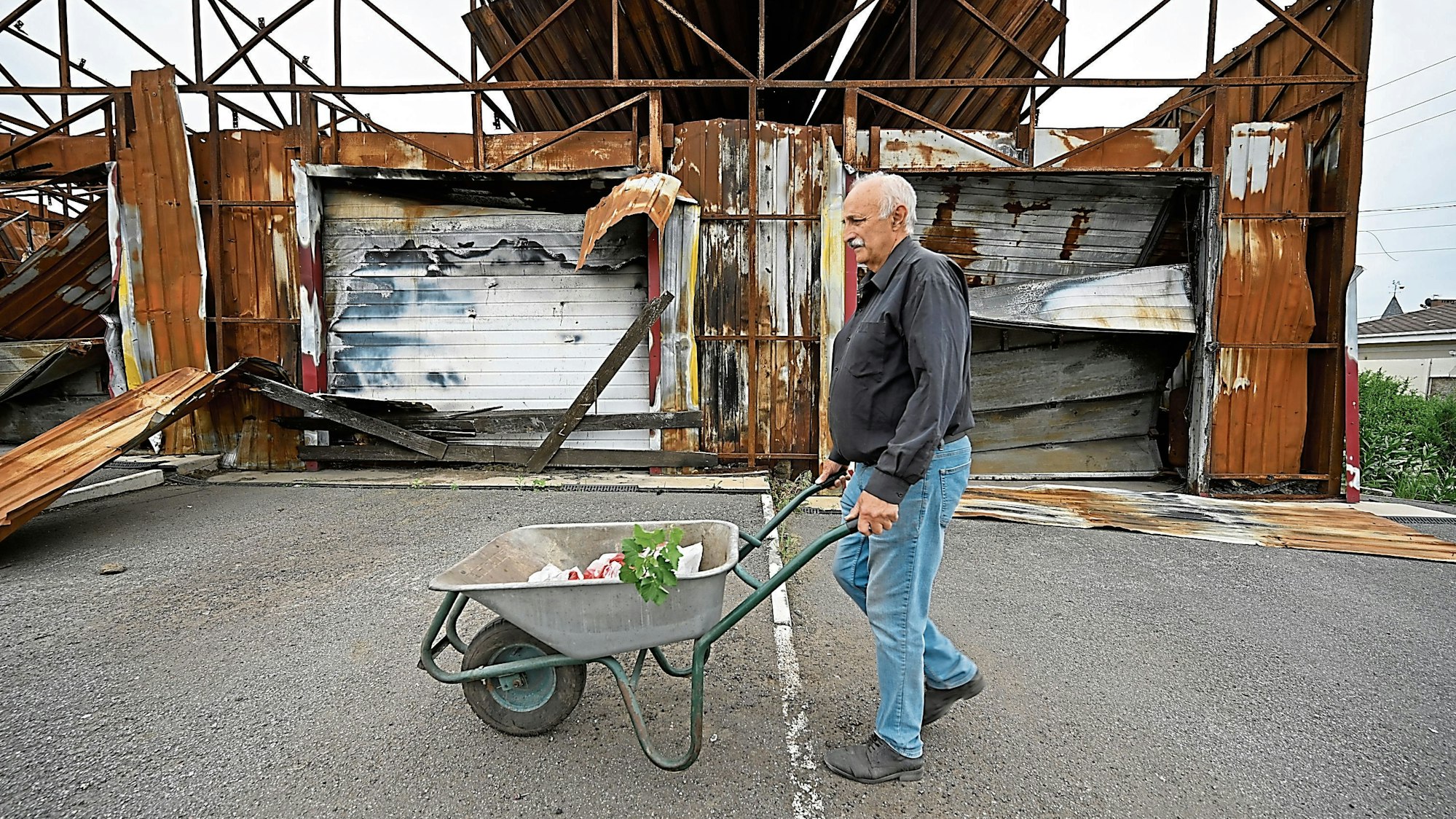 Serhij Kaljuzhnyj will bleiben: Mit seiner Schubkarre geht er an einer zerstörten Autowaschanlage vorbei.