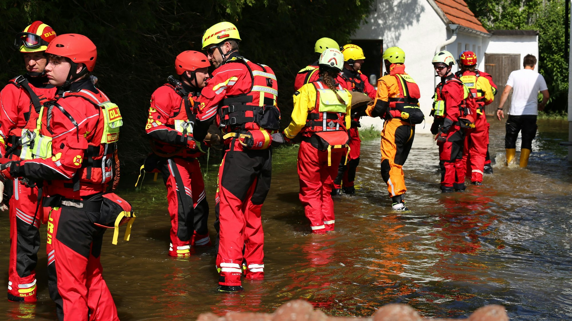 DLRG-Retter reichen in einer Menschenkette Sandsäcke weiter durchs knöchelhohe Wasser auf einer überfluteten Straße.