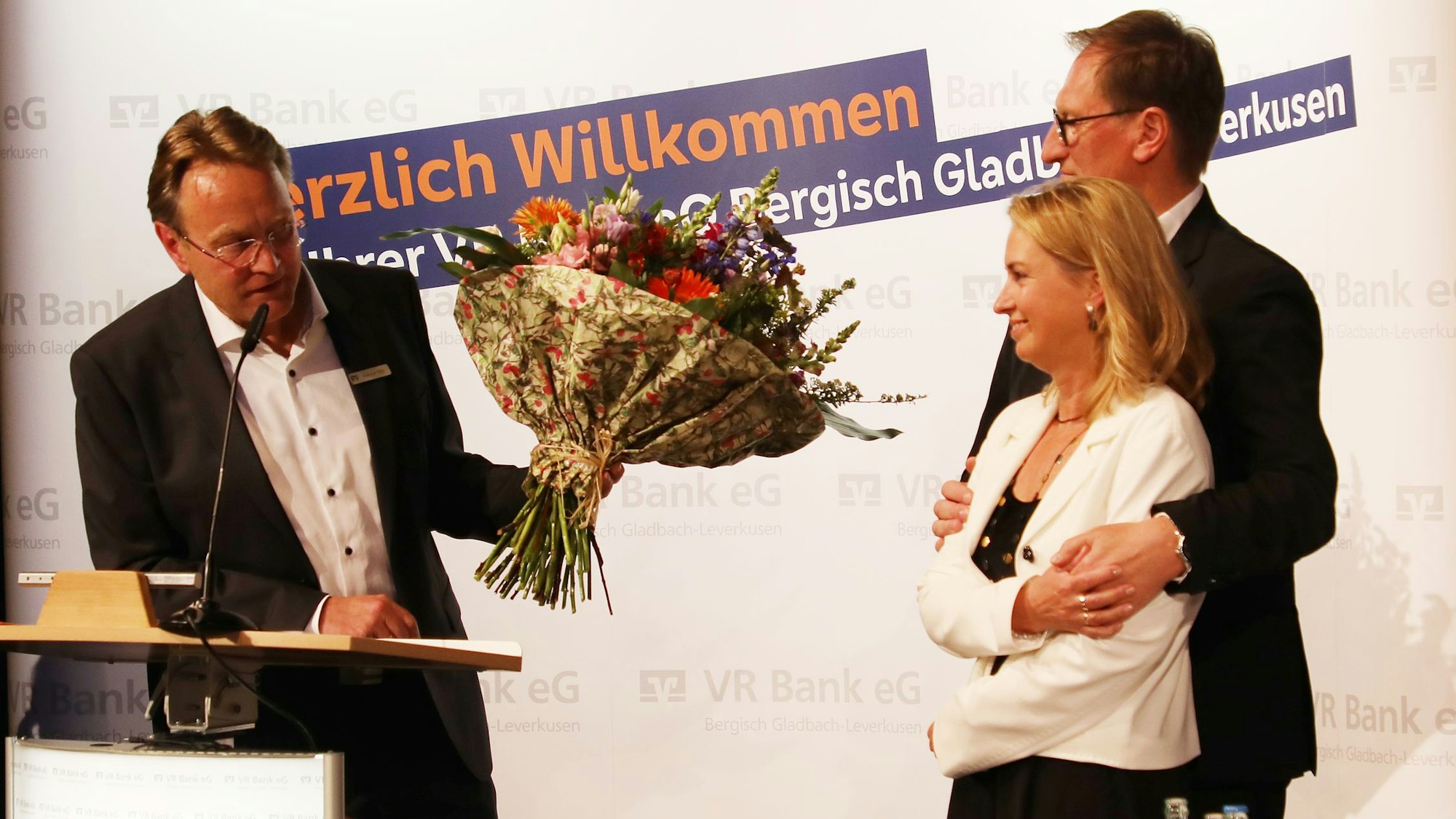 Ein Mann überreicht einen Blumenstrauß an ein Paar auf der Bühne des Bürgerhauses Bergischer Löwe.