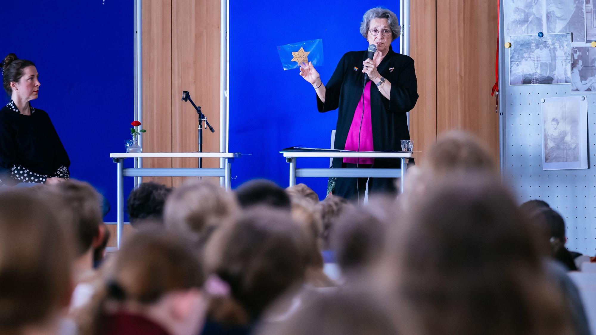 Eine Frau mit einem Davidstern in der Hand steht auf einer Bühne vor Kindern.