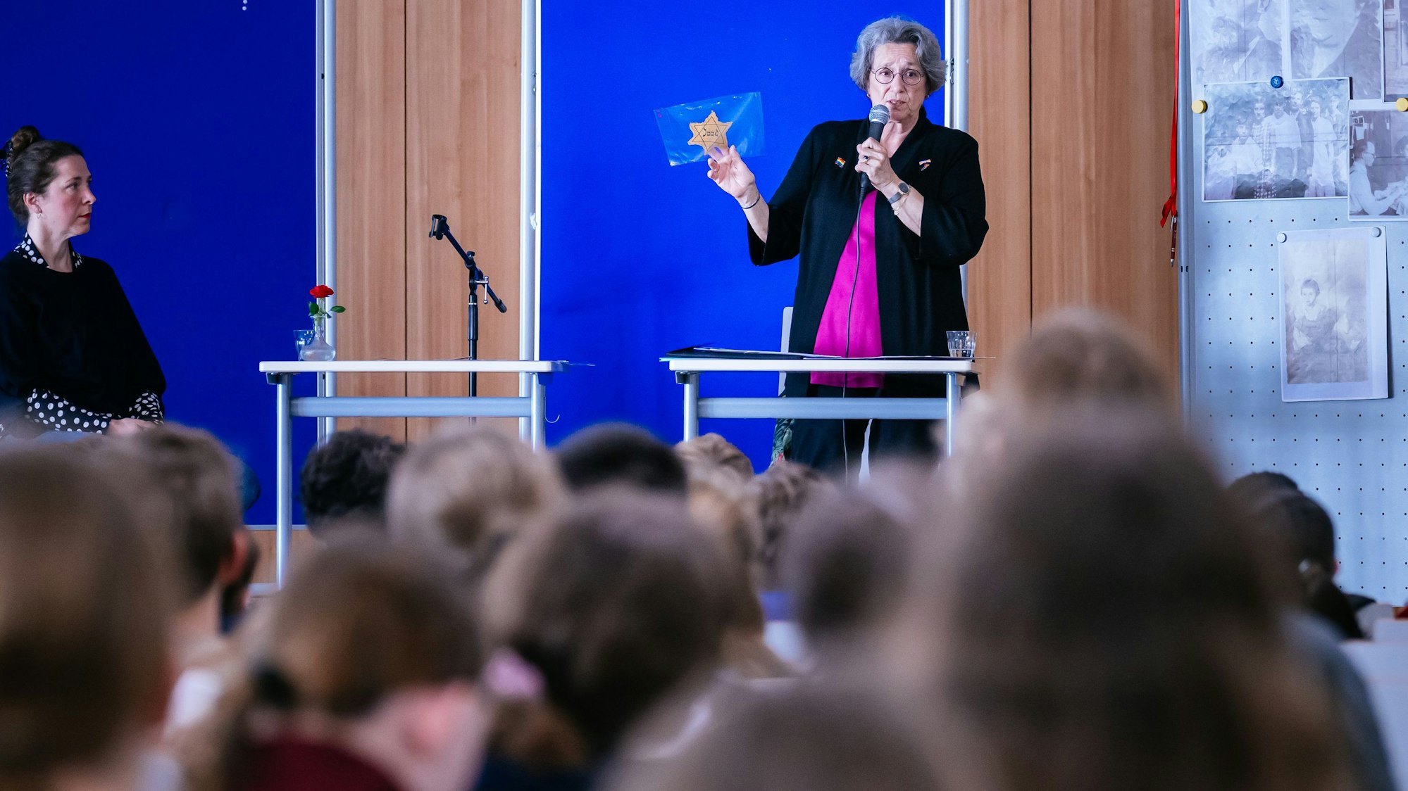 Eine Frau mit einem Davidstern in der Hand steht auf einer Bühne vor Kindern.