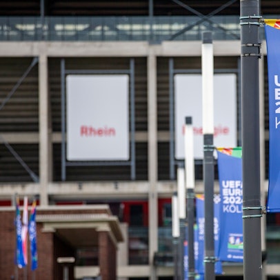 Am Rhein Energie Stadion hängen Fahnen, die auf die Fußball-EM hinweisen.