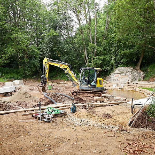 Ein gelber Bagger steht auf einer Baustelle im Wald: Hier wird bei Nettersheim-Holzmülheim der Park an der Erftquelle umgebaut.