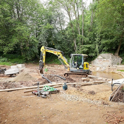 Ein gelber Bagger steht auf einer Baustelle im Wald: Hier wird bei Nettersheim-Holzmülheim der Park an der Erftquelle umgebaut.
