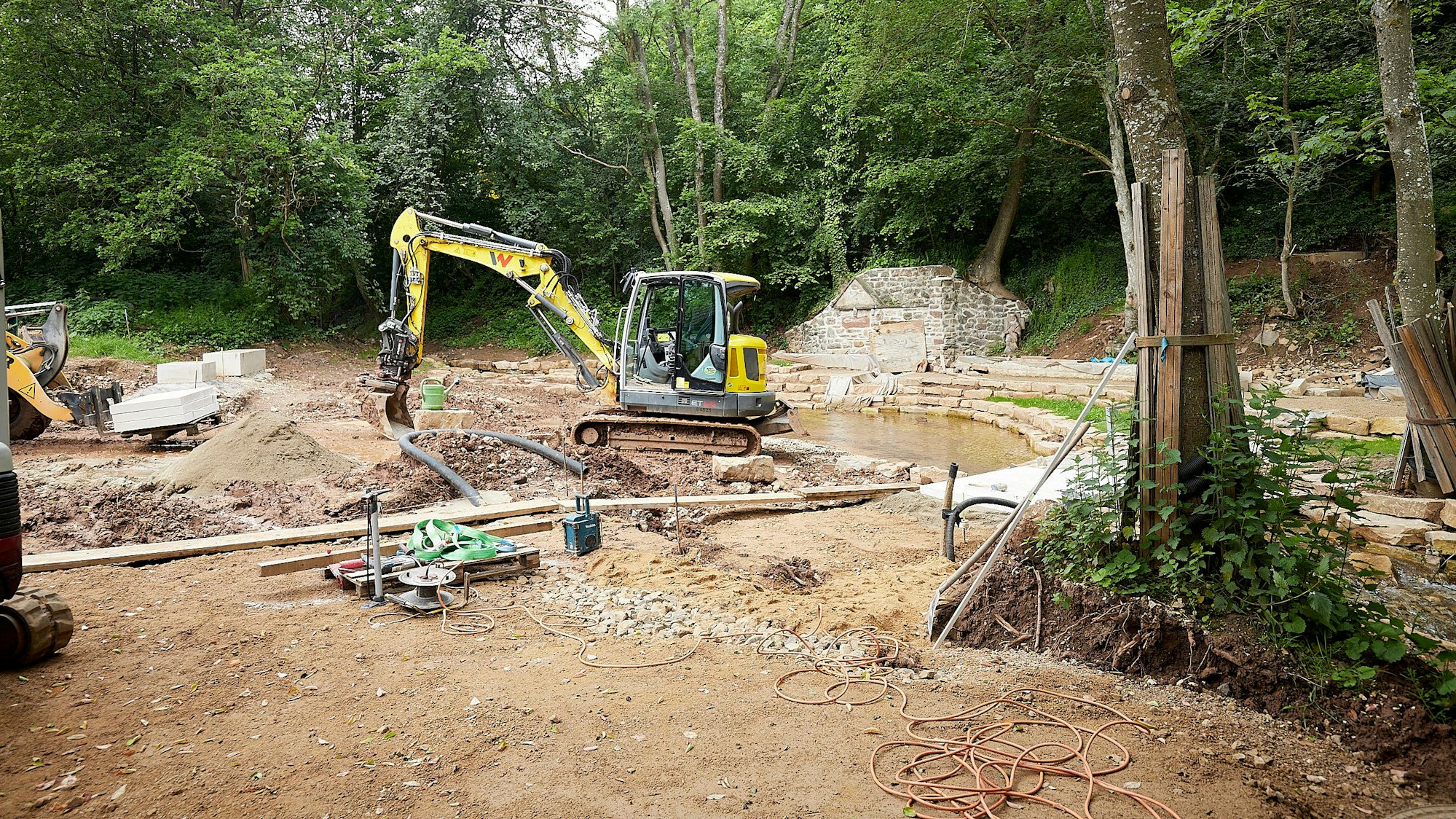 Ein gelber Bagger steht auf einer Baustelle im Wald: Hier wird bei Nettersheim-Holzmülheim der Park an der Erftquelle umgebaut.