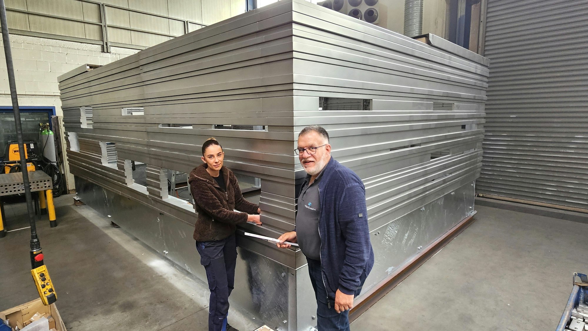 Alina Nettekoven und Michael Schneider stehen vor der Einhausung aus Edelstahl, die sich noch in den Kalller Werkshallen befindet.