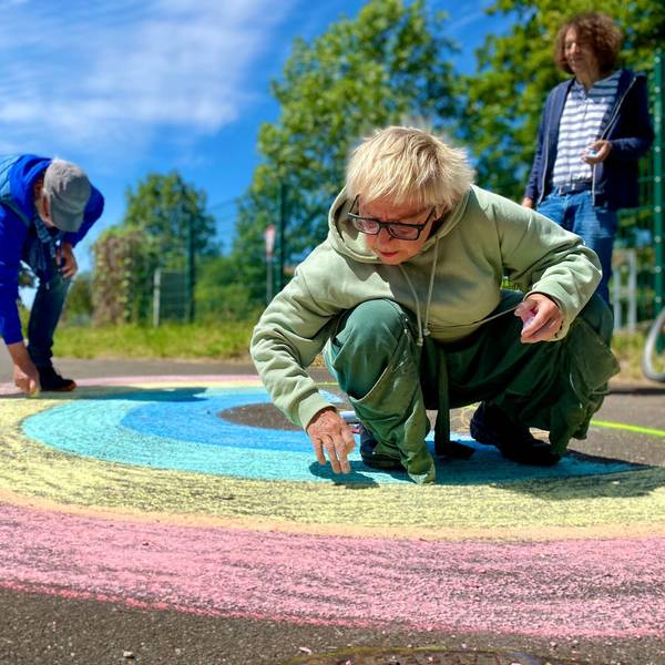 Anne Bergmann, Leo Schmidt und Thomas Latzke malen mit Straßenkreide einen Regenbogen auf die Straße.