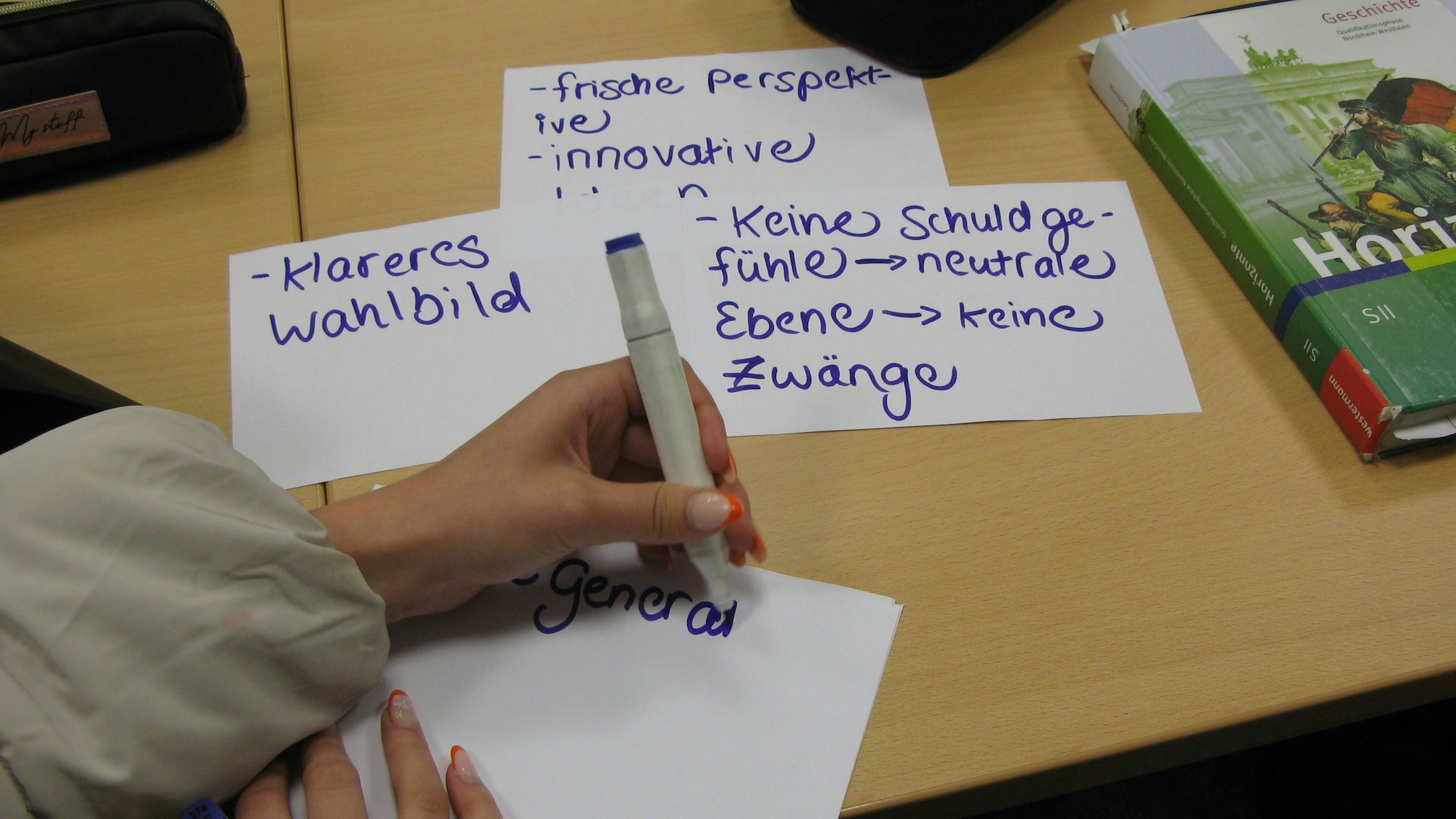Eine Hand mit einem Stift: Eine Schülerin notiert Stichworte auf Karteikarten.